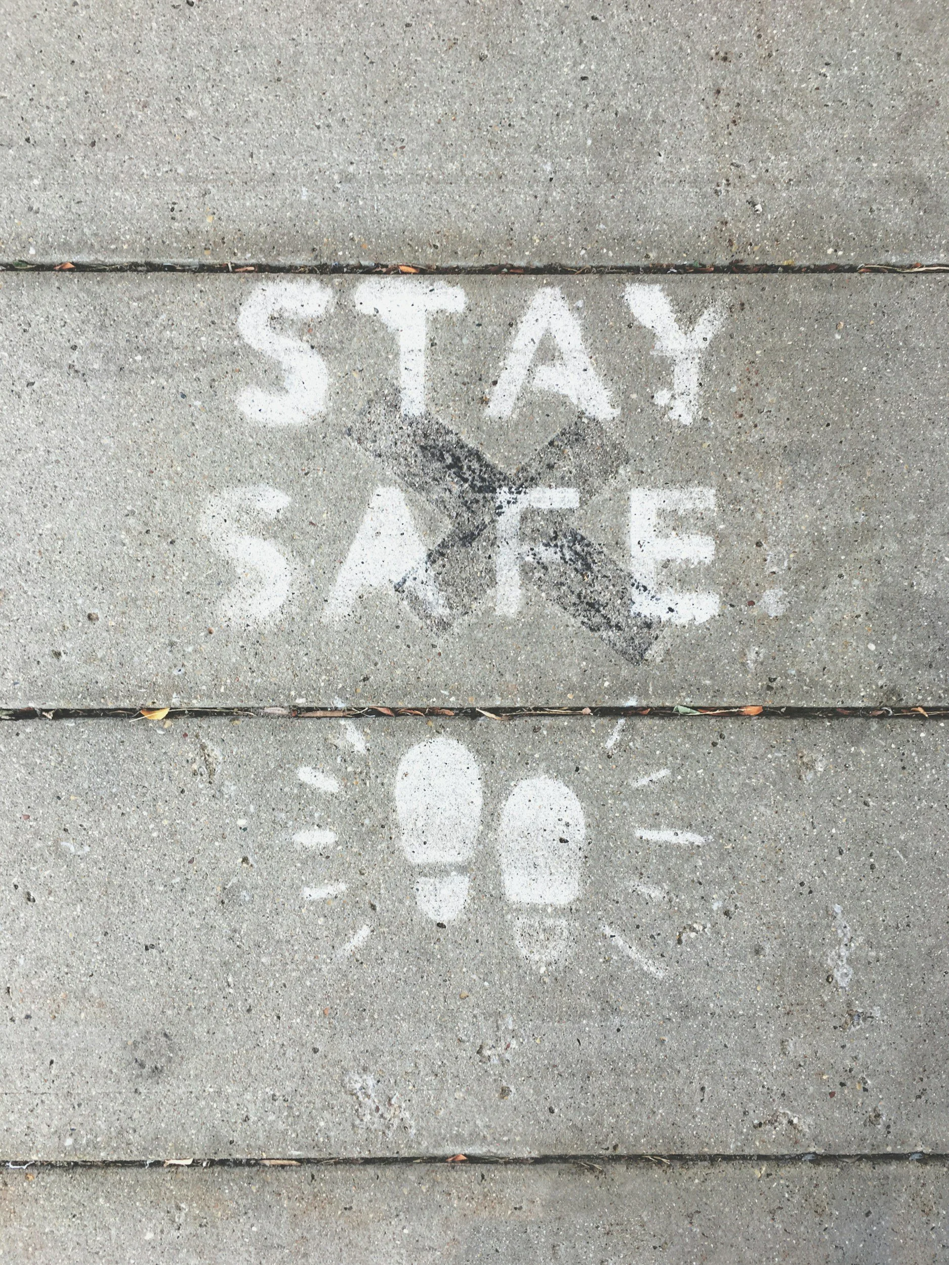 Concrete sidewalk with white chalk markings that say 'STOP' and 'SAFE' with a painted image of footsteps.