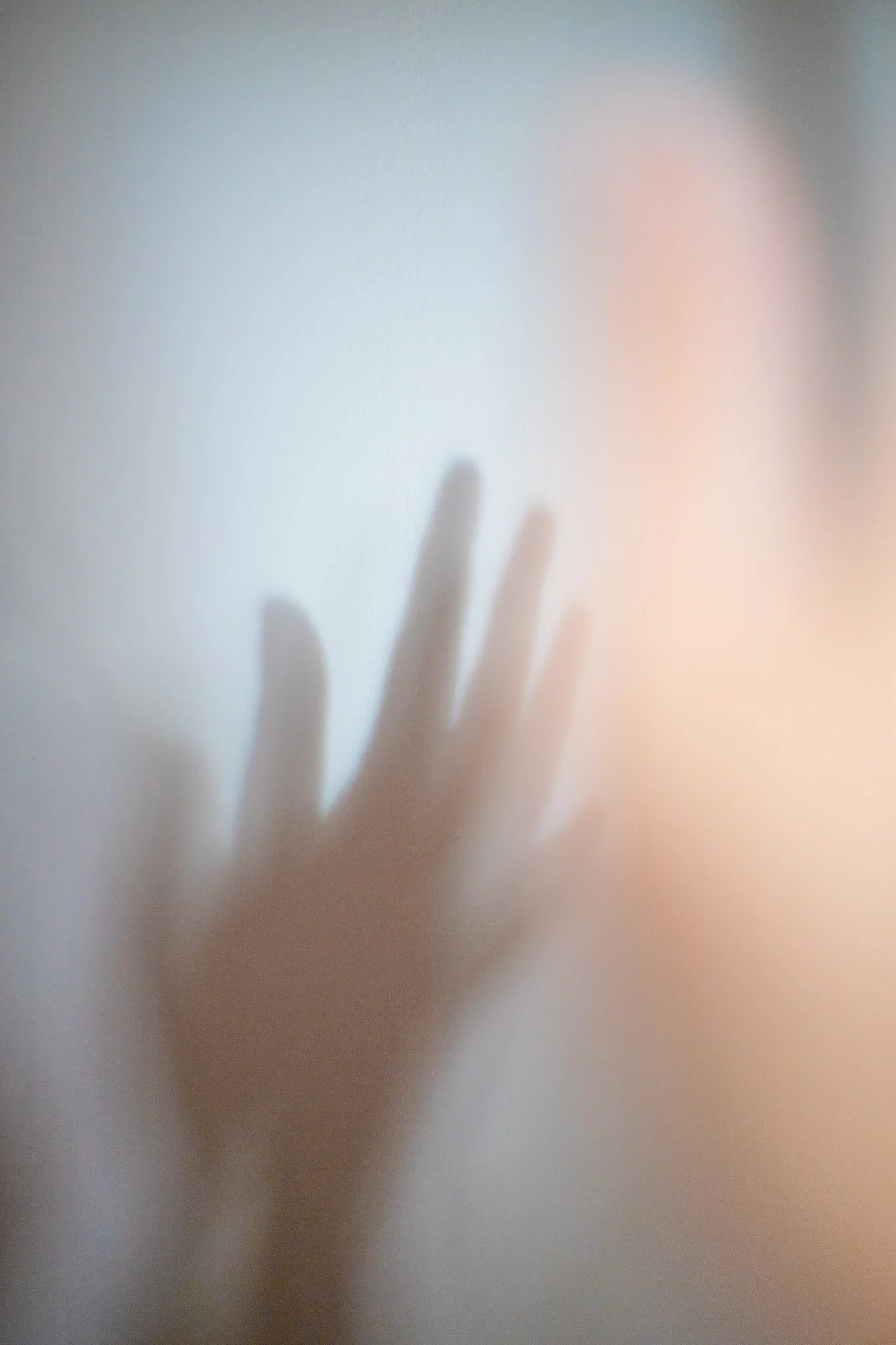 Une main floue appuyant contre une surface translucide ou une fenêtre, créant une ombre sur le mur derrière.