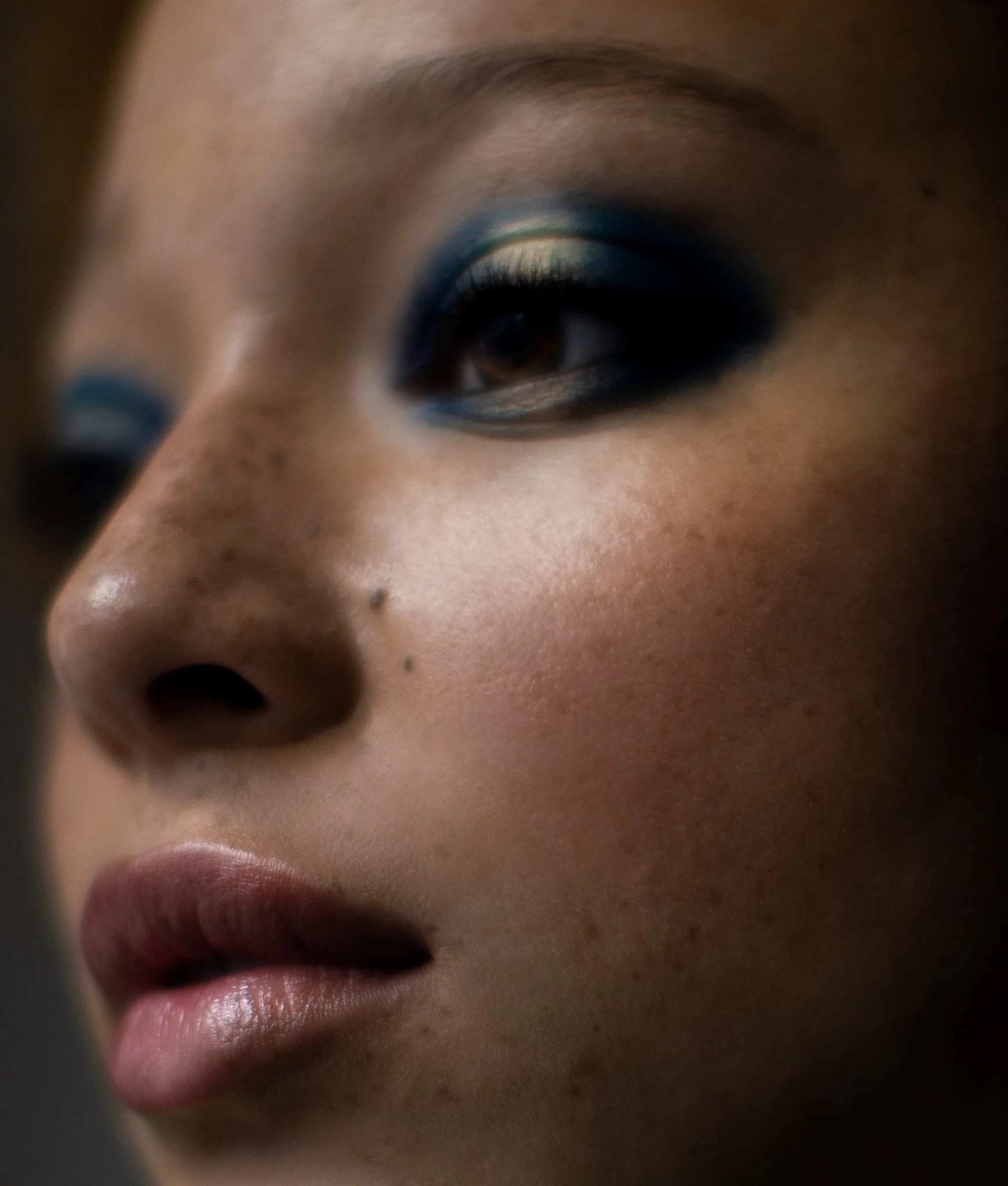 Un gros plan du visage d'une femme, mettant en valeur ses yeux maquillés avec du bleu et ses lèvres naturelles.