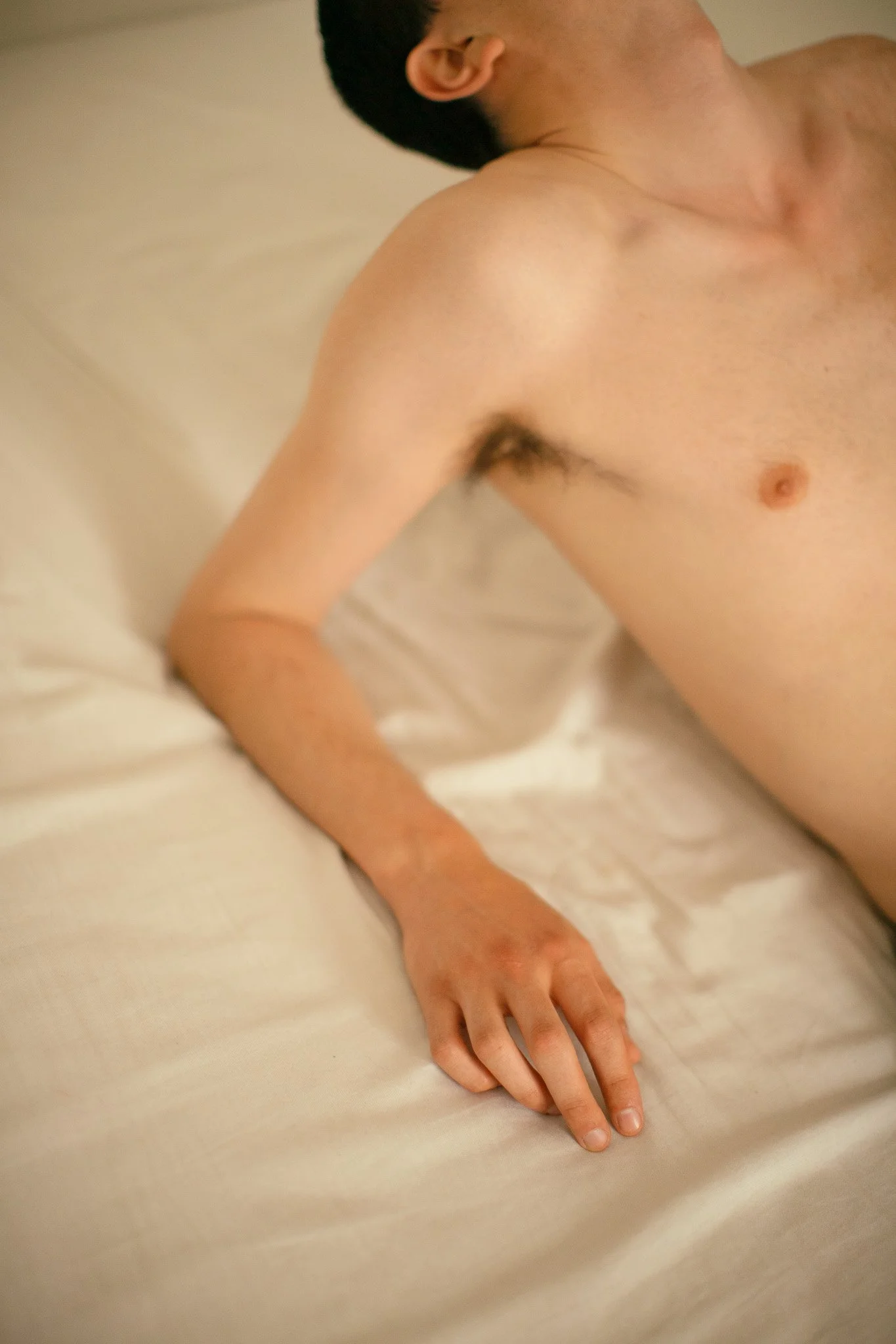 Un homme nu allongé sur un lit, vu de côté, avec la tête tournée vers le haut, dans une pièce à éclairage doux.