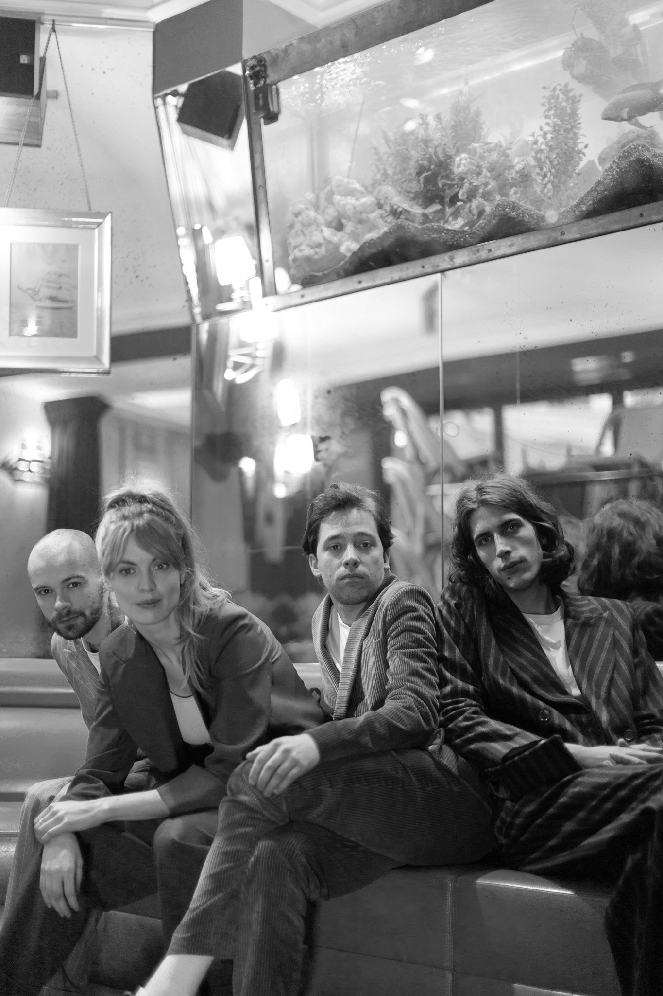 Quatre personnes assises sur un banc dans un café, avec un aquarium en arrière-plan.