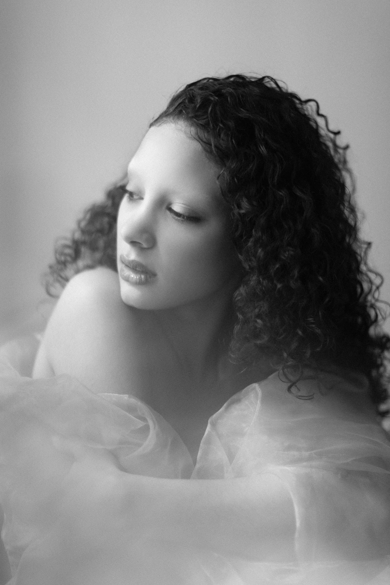 Portrait en noir et blanc d'une femme aux cheveux bouclés, regardant vers la gauche, vêtue d'une robe en tissu léger.