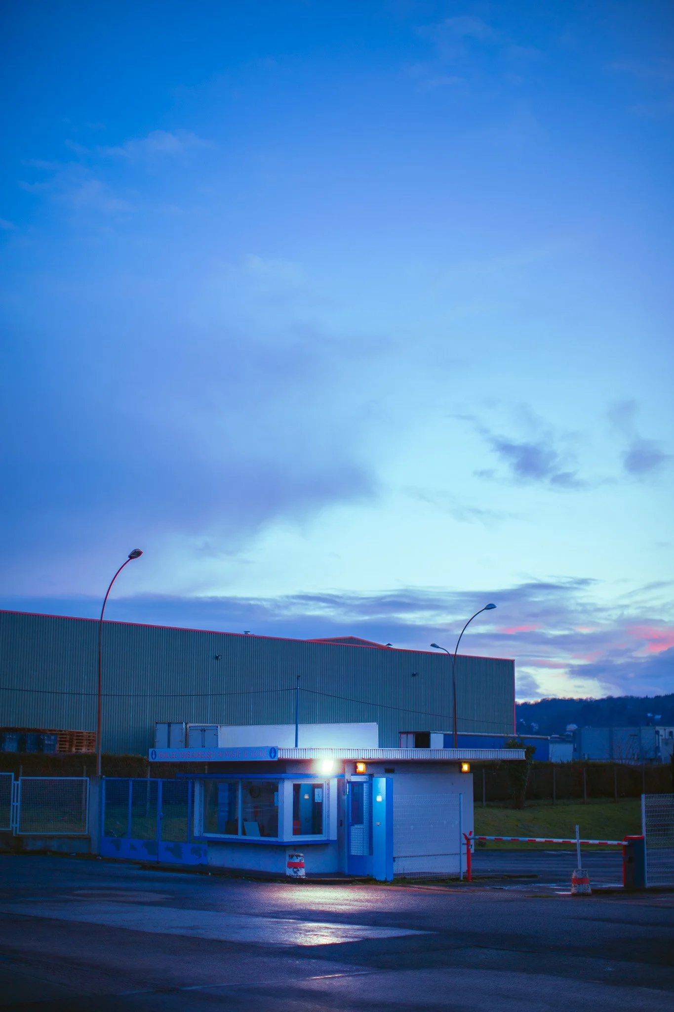 Une entrée de parking ou de zone de contrôle avec un bâtiment sous un ciel crépusculaire.