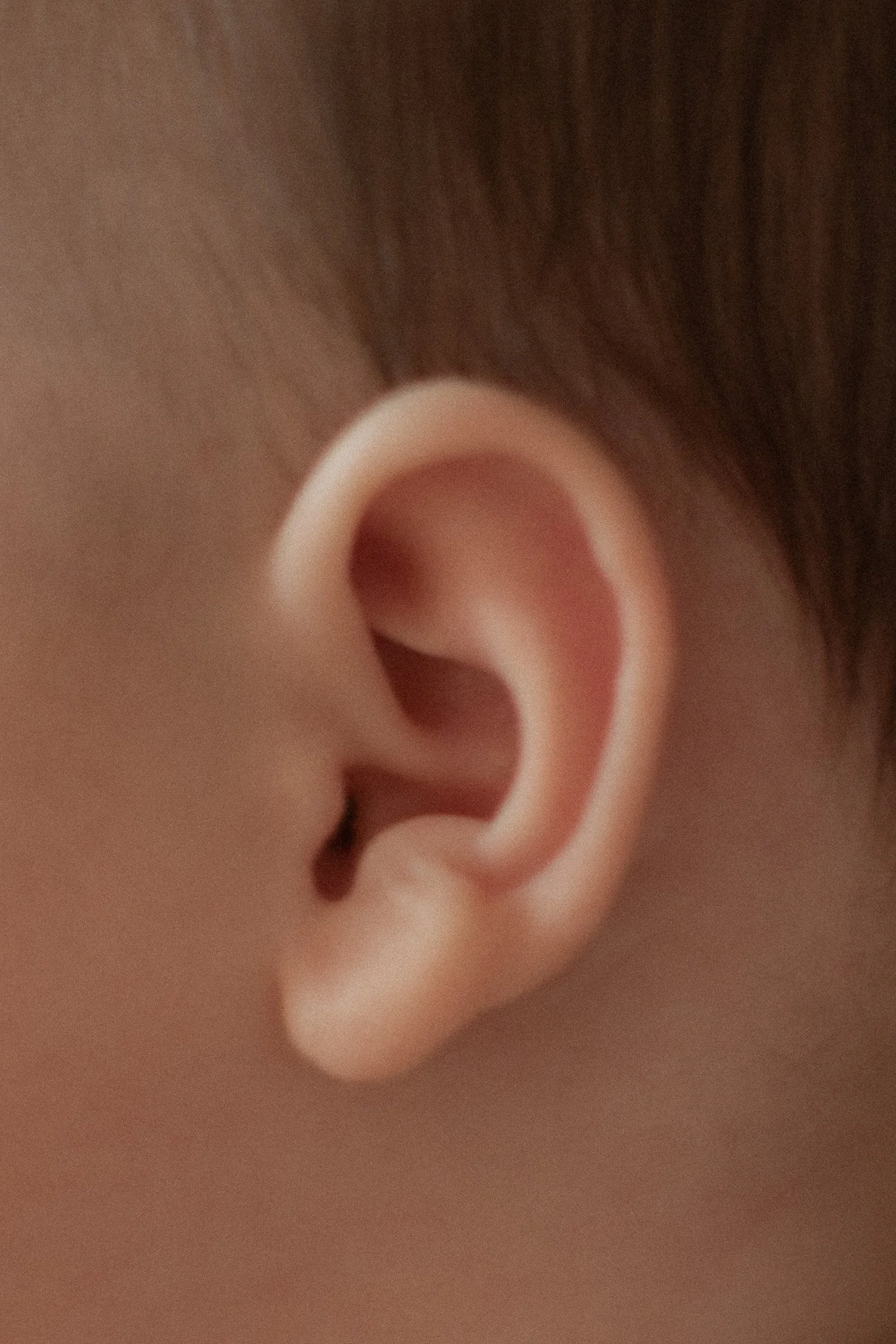 Une oreille humaine de près, avec des détails visibles de la peau et des cheveux autour.