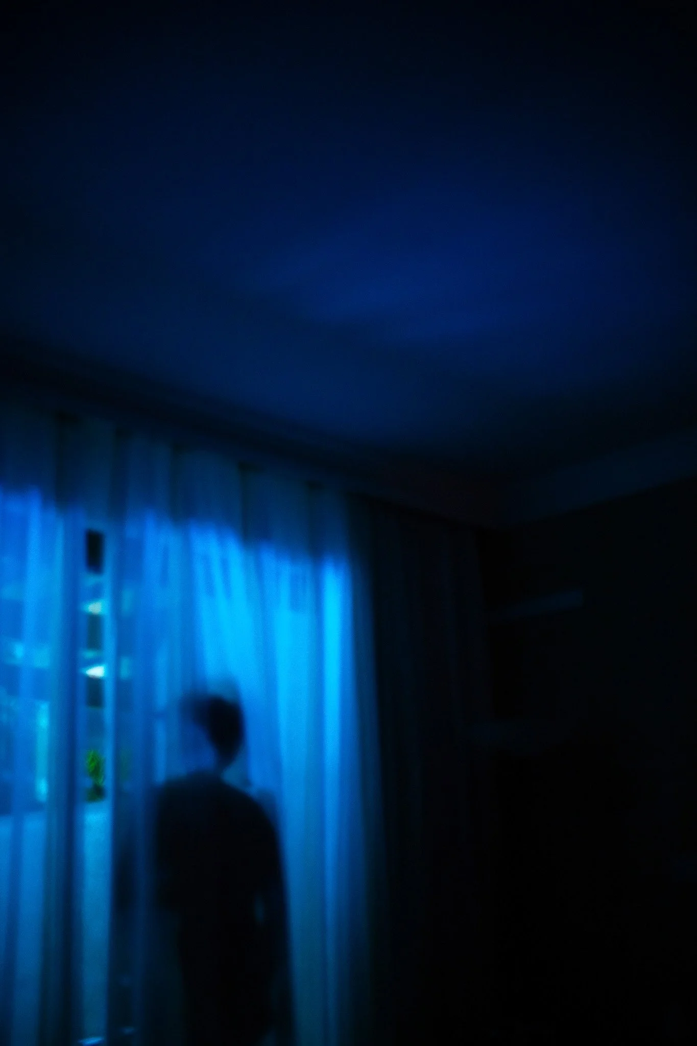 Silhouette d'une personne debout près de fenêtres avec rideaux bleus dans une pièce sombre