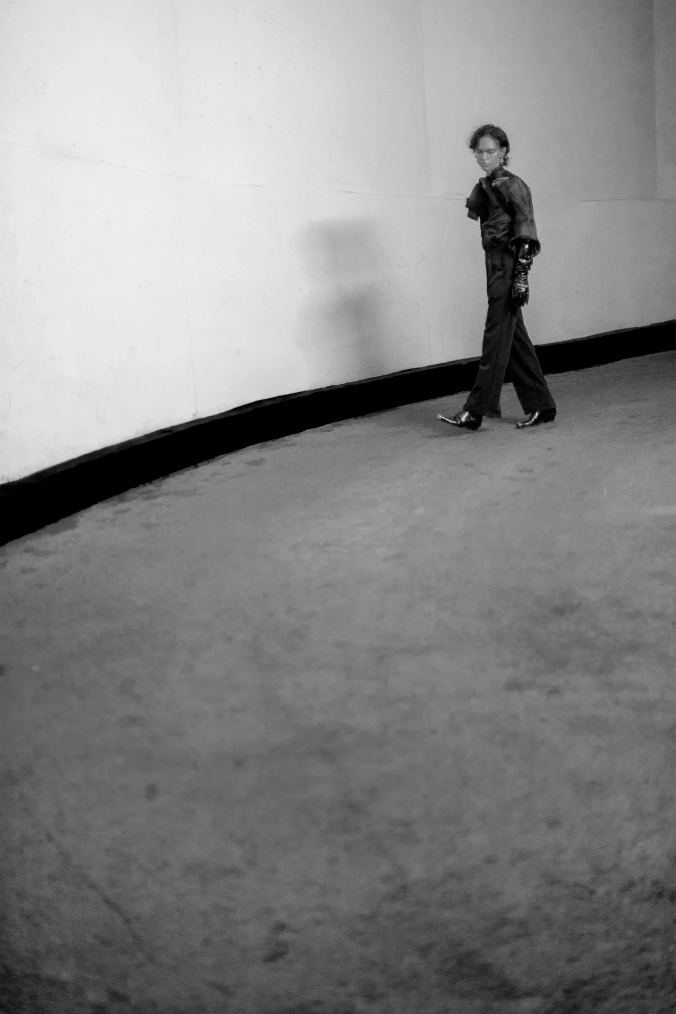 Une femme marche dans un couloir en noir et blanc, portant une tenue élégante et des chaussures à talons.