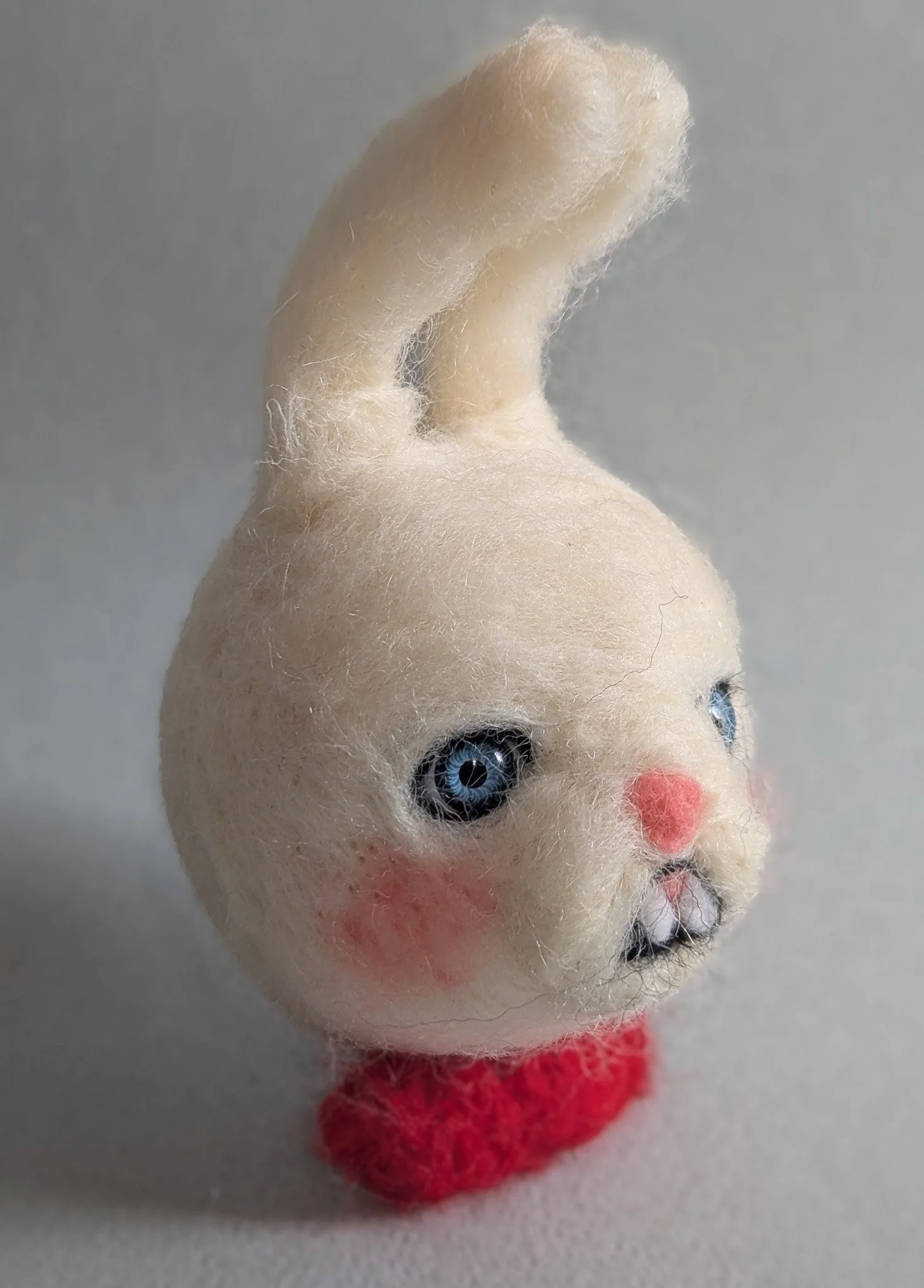 Une peluche de forme ronde avec un visage de chat, des yeux bleus, un nez rose, et un bouche avec des dents, sur un fond neutre.