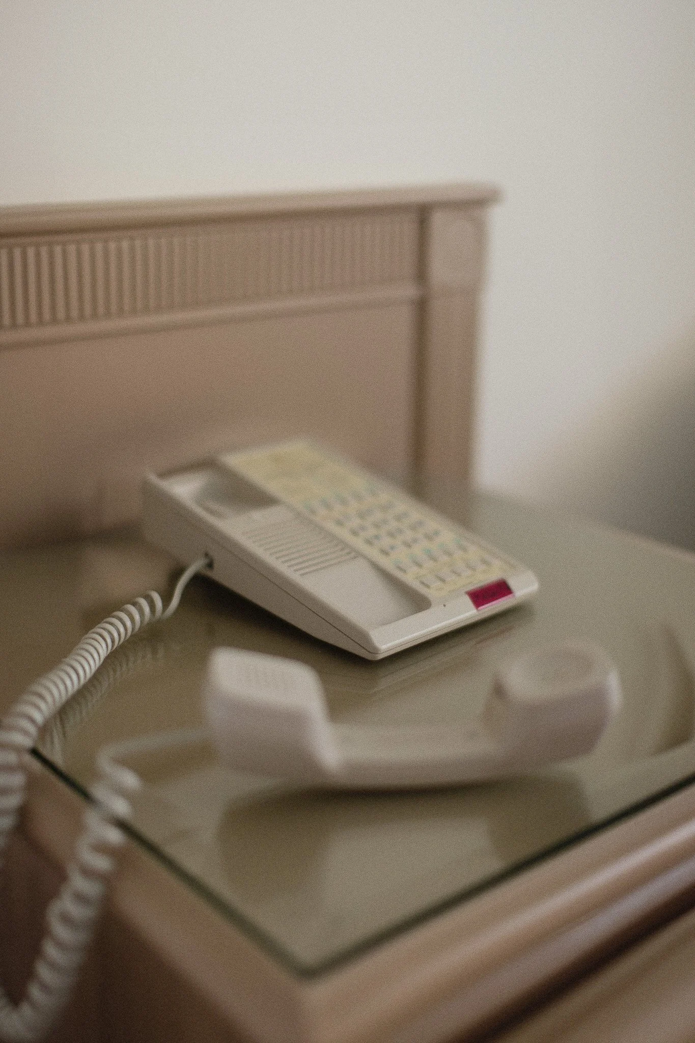 Téléphone fixe traditionnel et combiné placé sur une table de chevet en contexte de chambre d'hôtel ou chambre à coucher, dans un décor minimaliste.