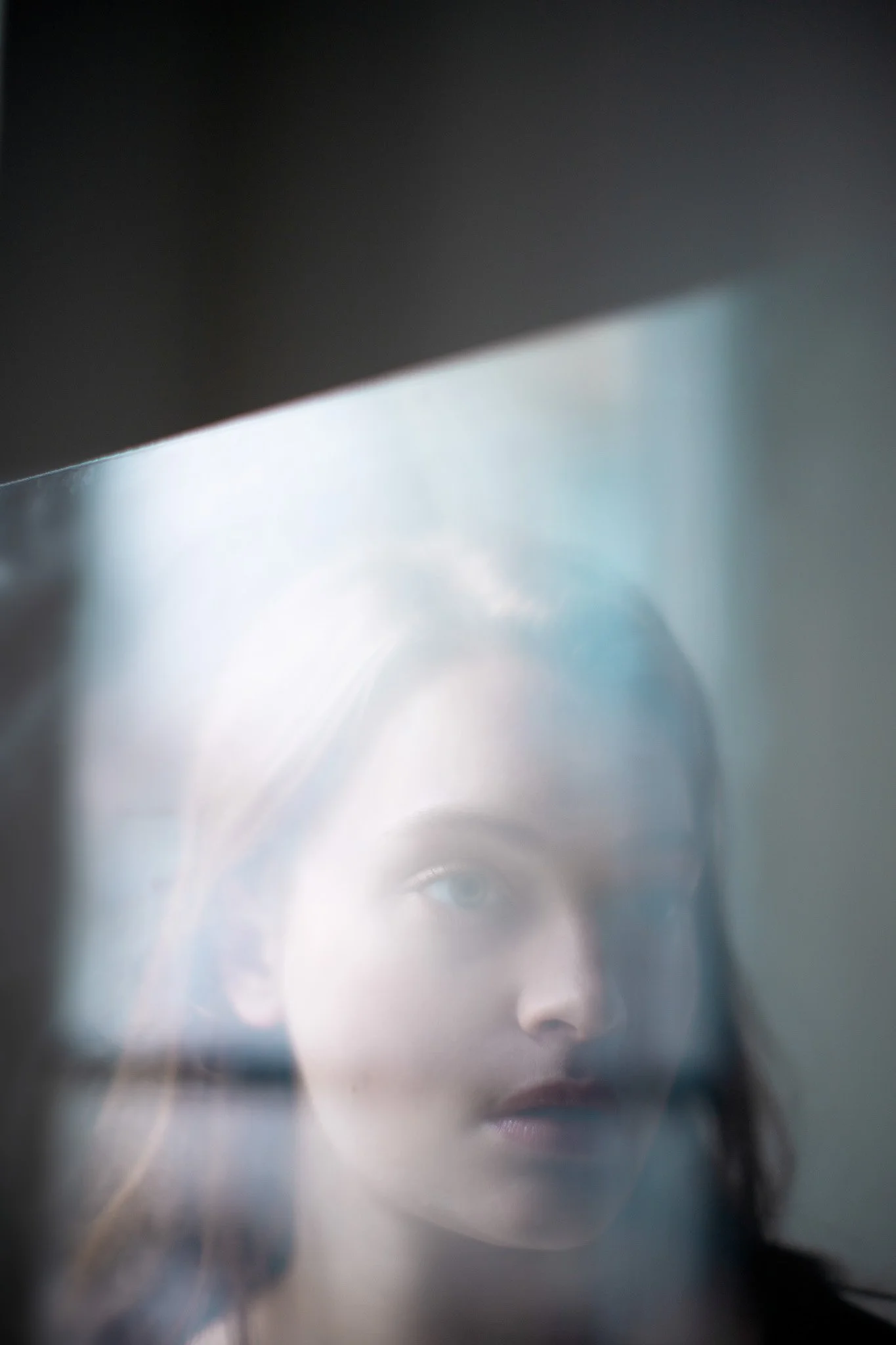 Portrait d'une femme avec reflet flou et éclairage doux, vue à travers une surface transparente.