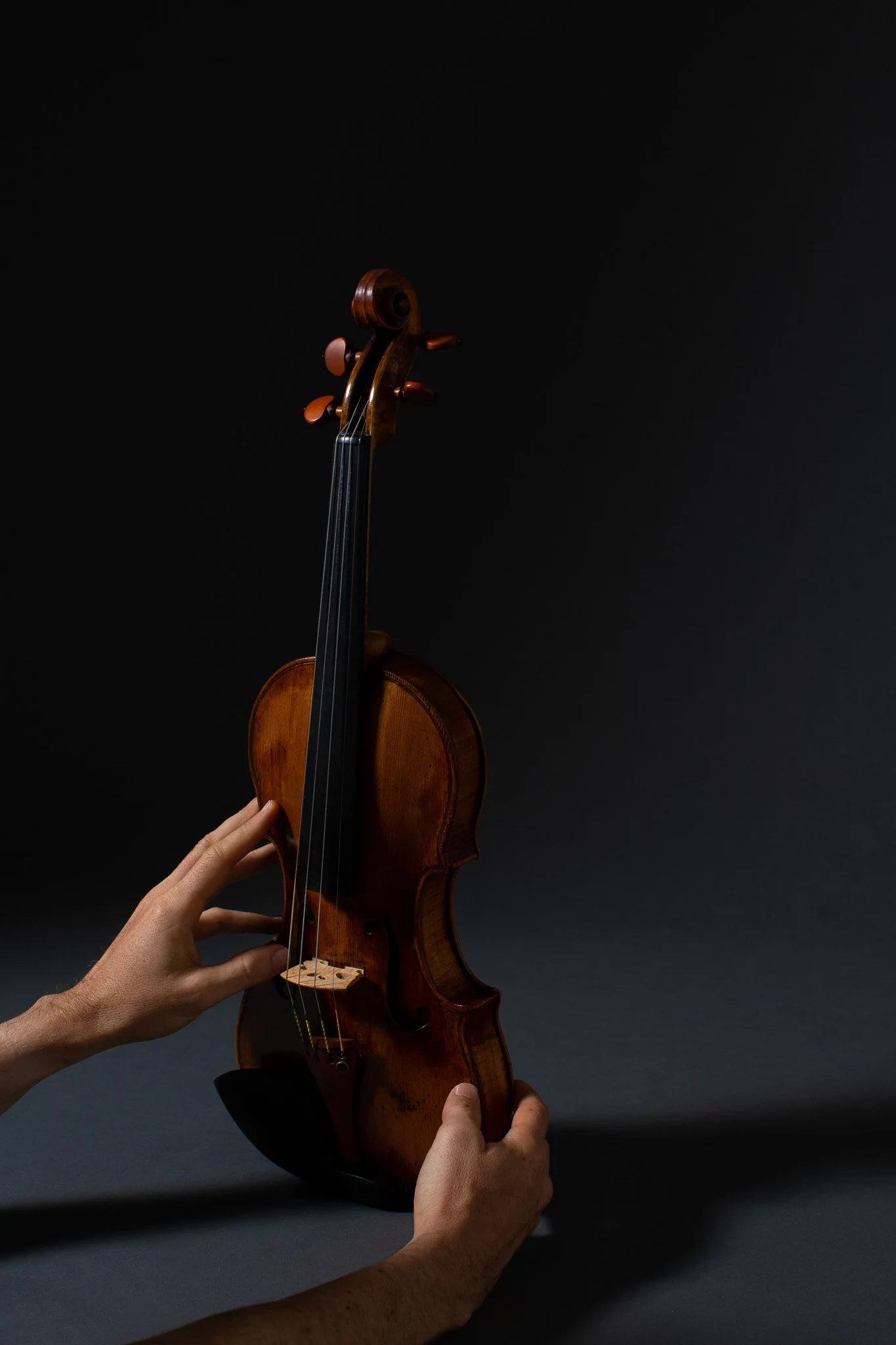 Deux mains tenant un violon en bois brun sur un fond sombre.