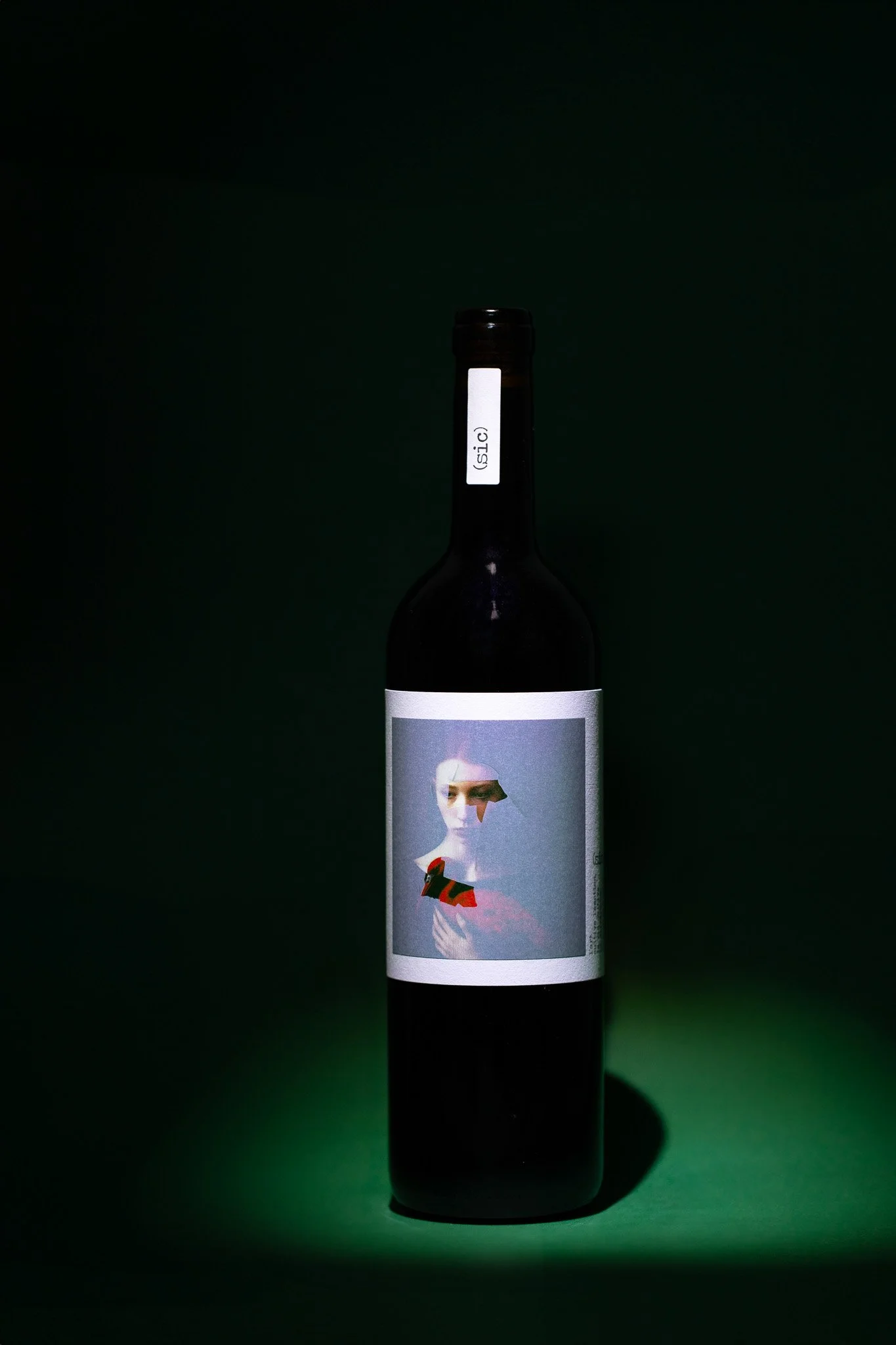 Bouteille de vin noire avec étiquette artistique d'une femme en rouge, derrière un fond vert foncé.