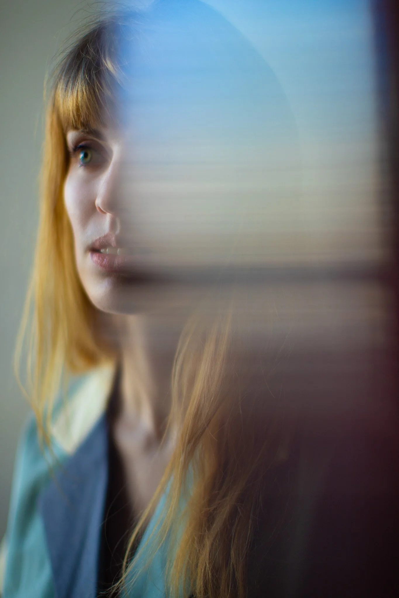 Une jeune femme aux cheveux roux regarde à travers une surface translucide, créant une séparation partielle dans l'image.