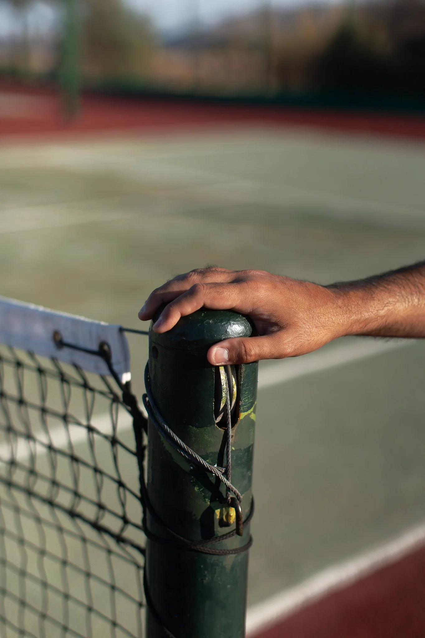 Main d'homme posée sur un poteau de filet de tennis au bord d'un court de tennis.