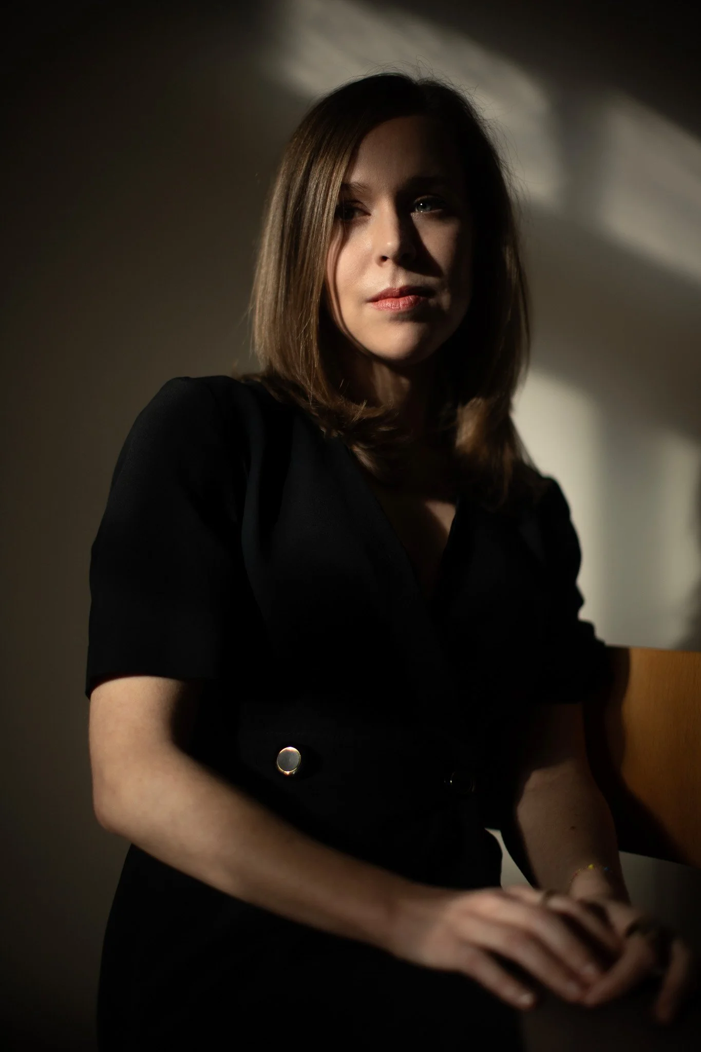 Portrait d'une femme avec des cheveux bruns, portant une tenue noire, dans un éclairage tamisé.