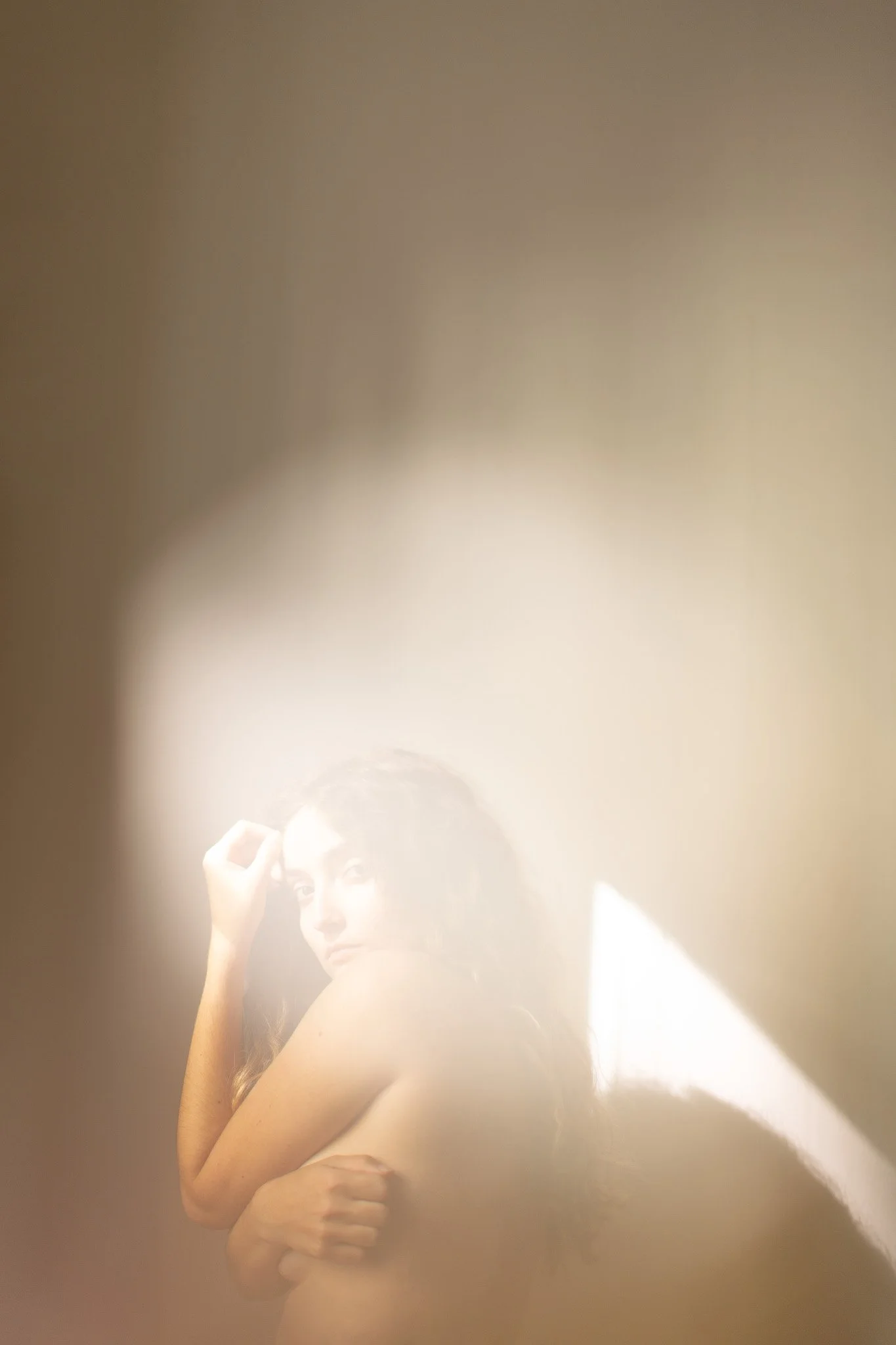 Une femme regardant à travers un miroir partiellement obscurci par une lumière douce.