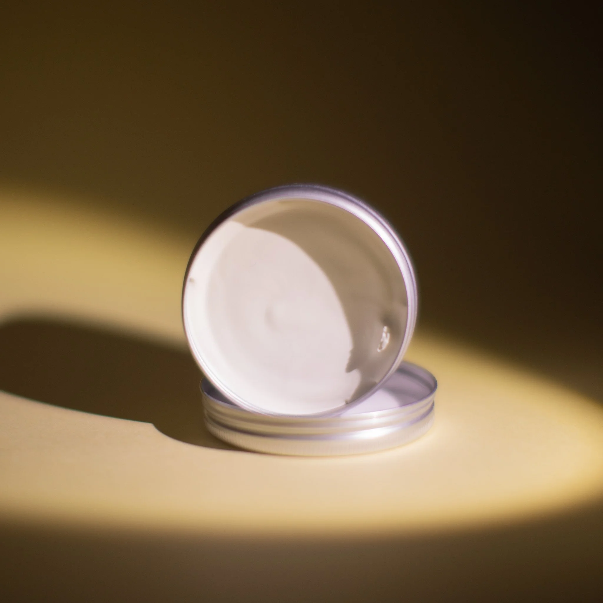 Un récipient en aluminium ouvert avec une substance blanche à l'intérieur, placé sur une surface jaune, avec un fond sombre.