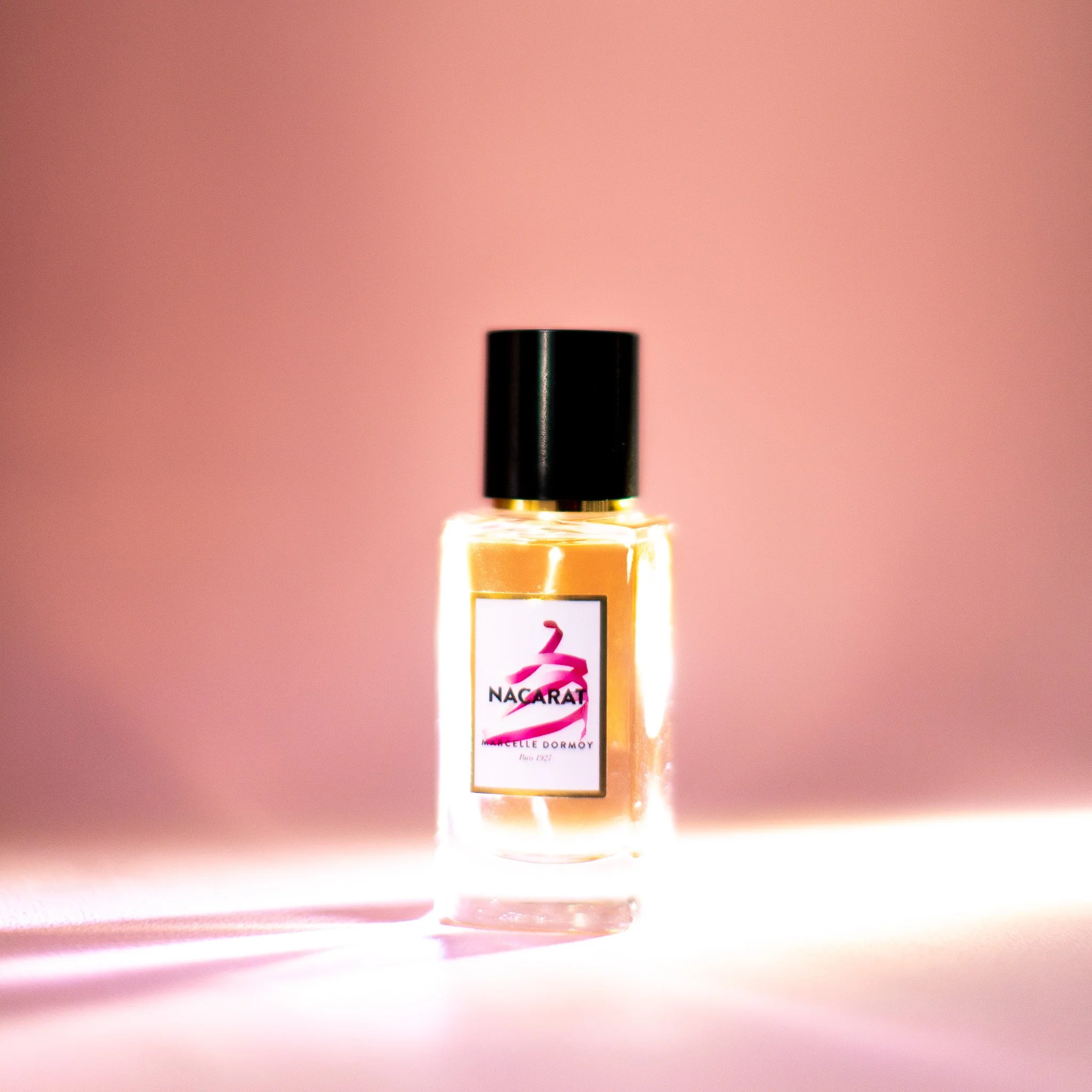 Une bouteille de parfum avec un fond rose. La bouteille porte une étiquette avec le logo "NAGARAT".