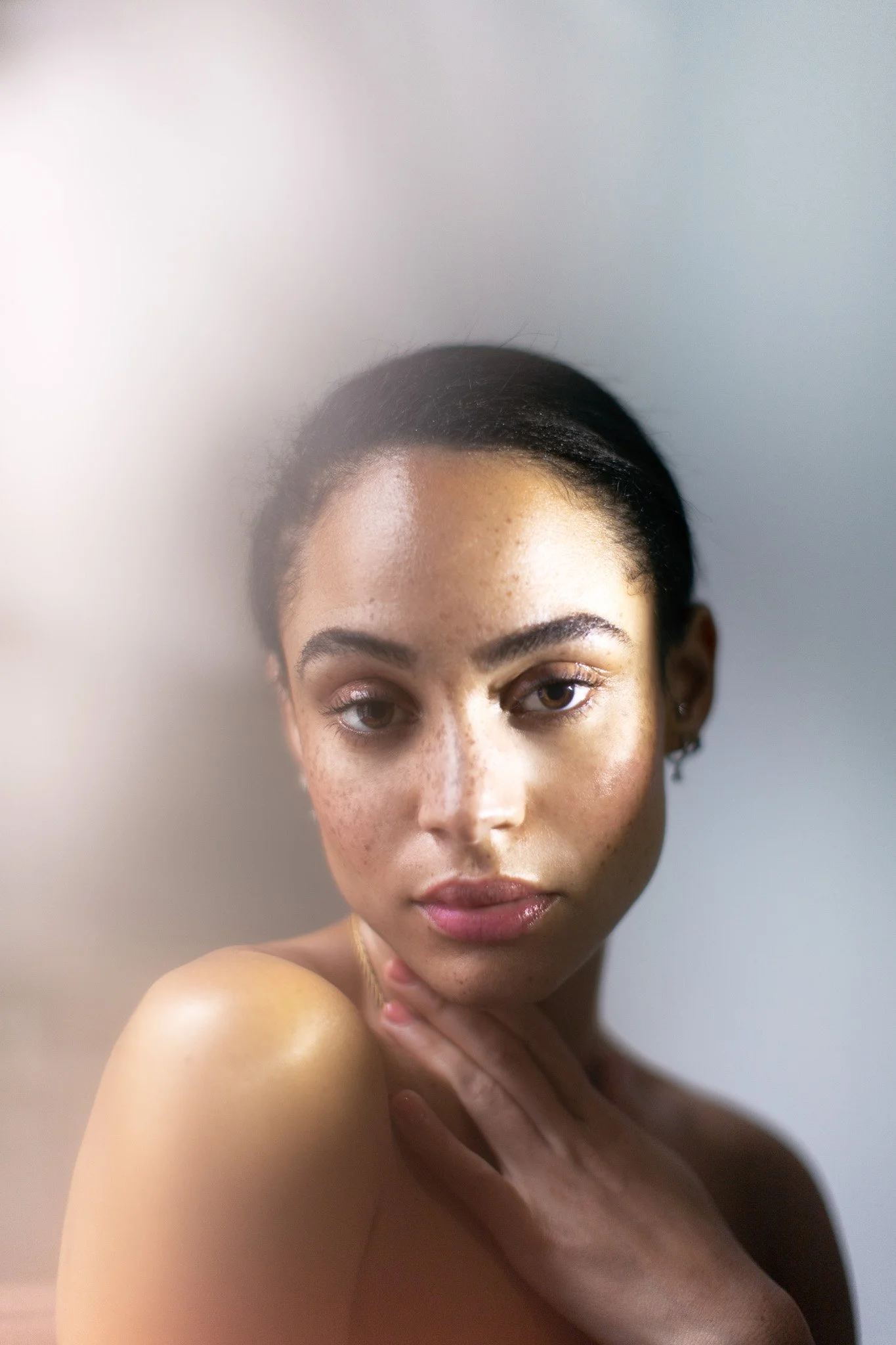 Portrait d'une femme avec peau claire et taches de pigmentation, regardant droit, chevelure sombre, fond neutre.