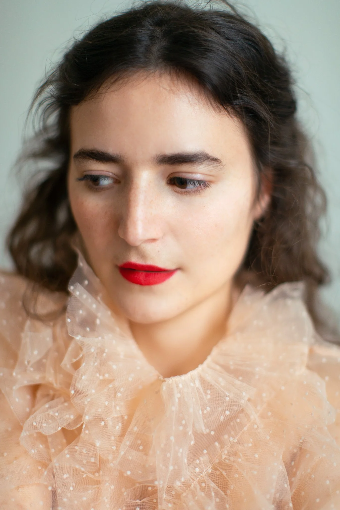 Jeune femme avec maquillage naturel, lèvres rouges, portant une robe en tulle beige à pois blancs.