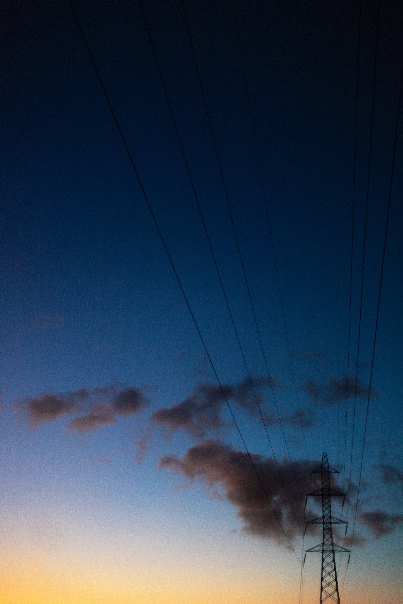 Ciel nocturne avec un pylône électrique et des fils électriques, quelques nuages dans le ciel.