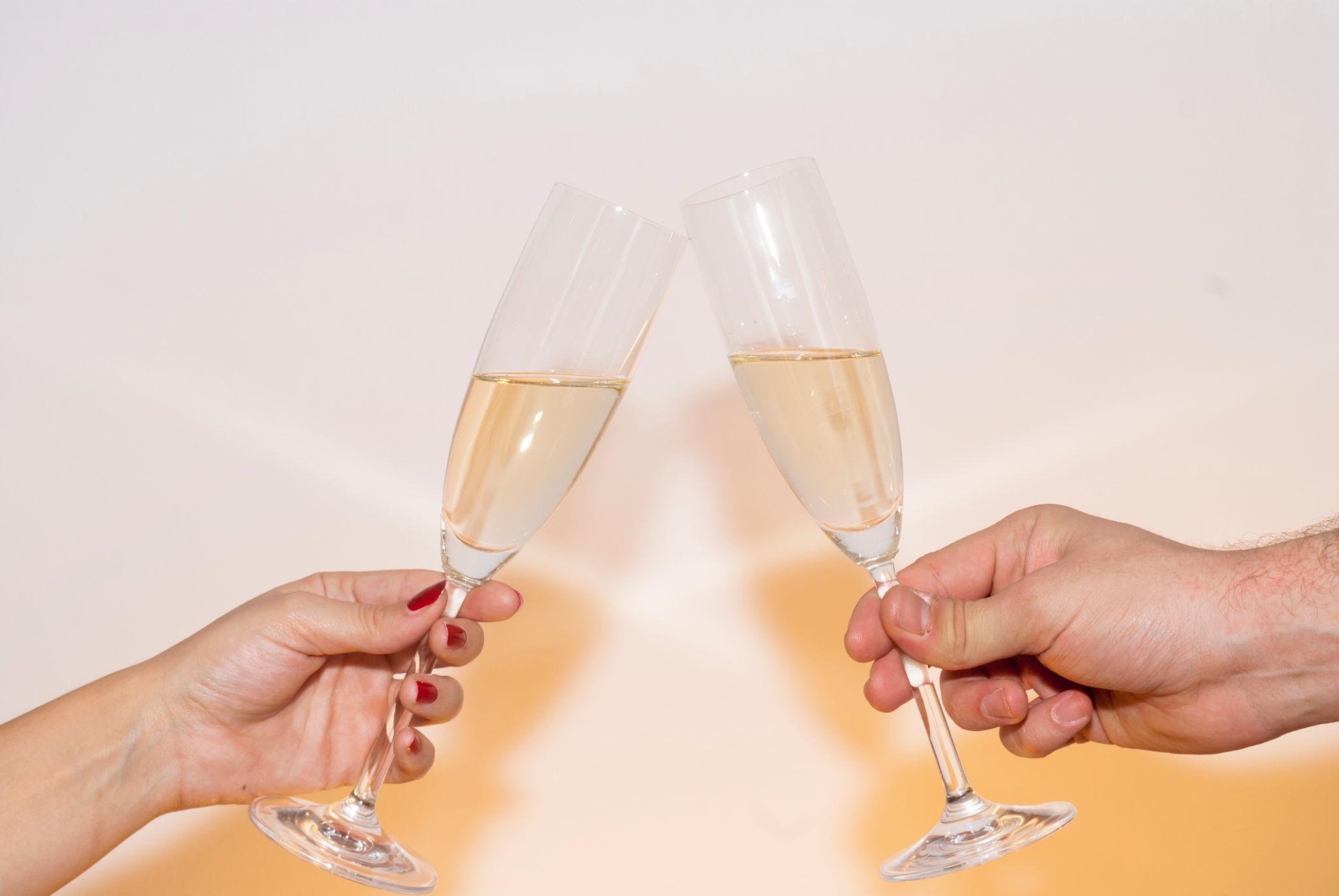 Two people clinking champagne glasses filled with a light-colored bubbly drink.