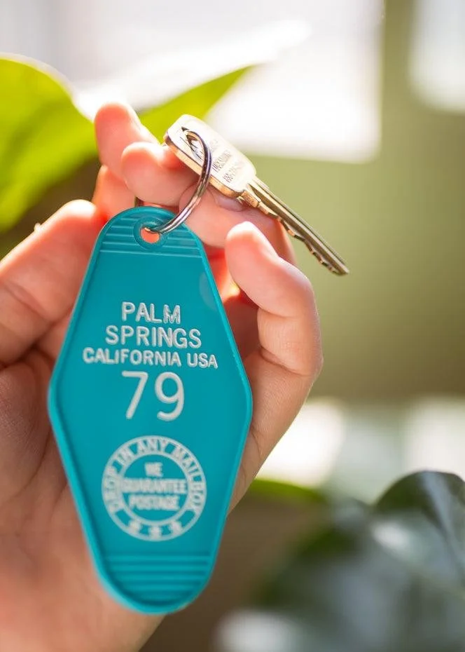 Close-up of a person's hand holding a keyring with a silver key and a blue tag marked 'Palm Springs California USA 79'.