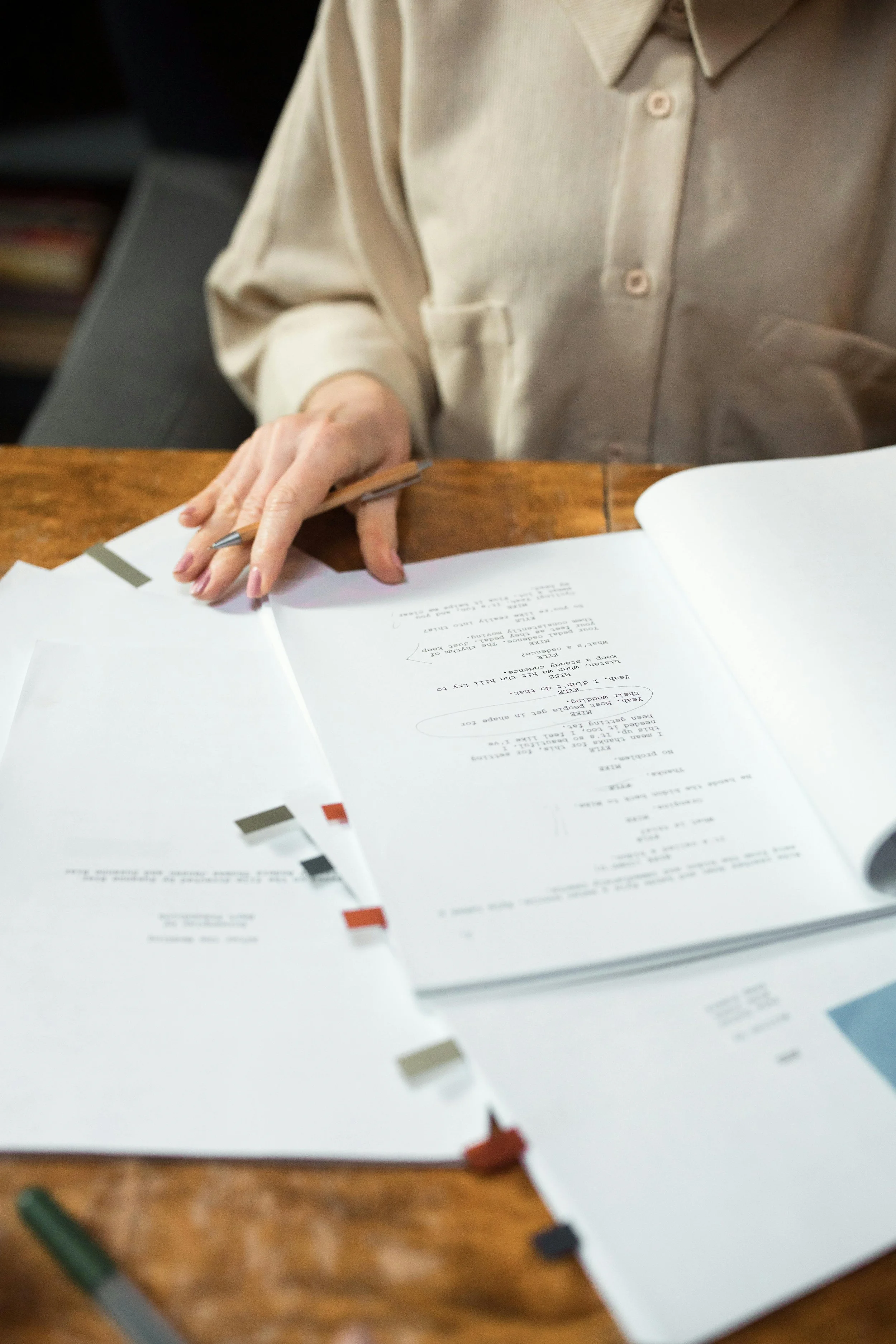 Una persona sta sfogliando un libro con testo e diagrammi, seduta a un tavolo di legno.