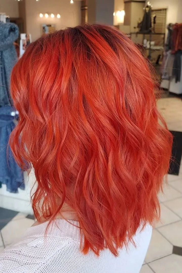 Woman with shoulder-length, wavy, bright orange-red hair in a salon or store setting.