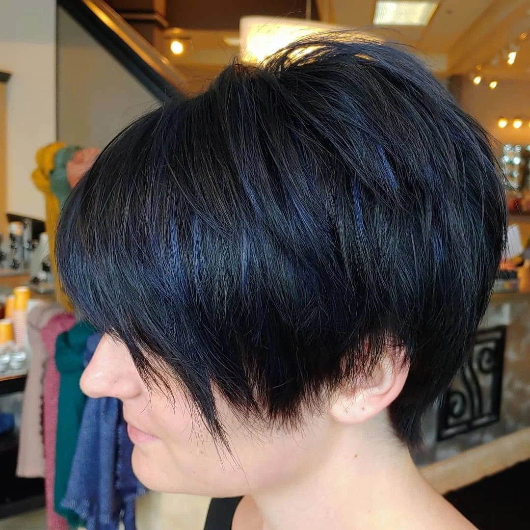 Side view of a person with short, layered black hair with blue highlights, in a hair salon.