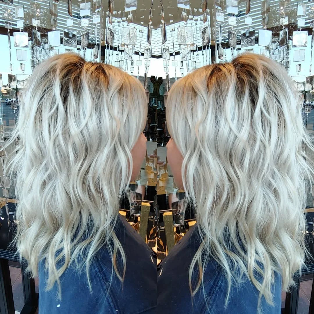 A mirror reflection of a woman with wavy blonde hair in a modern, art-filled space.