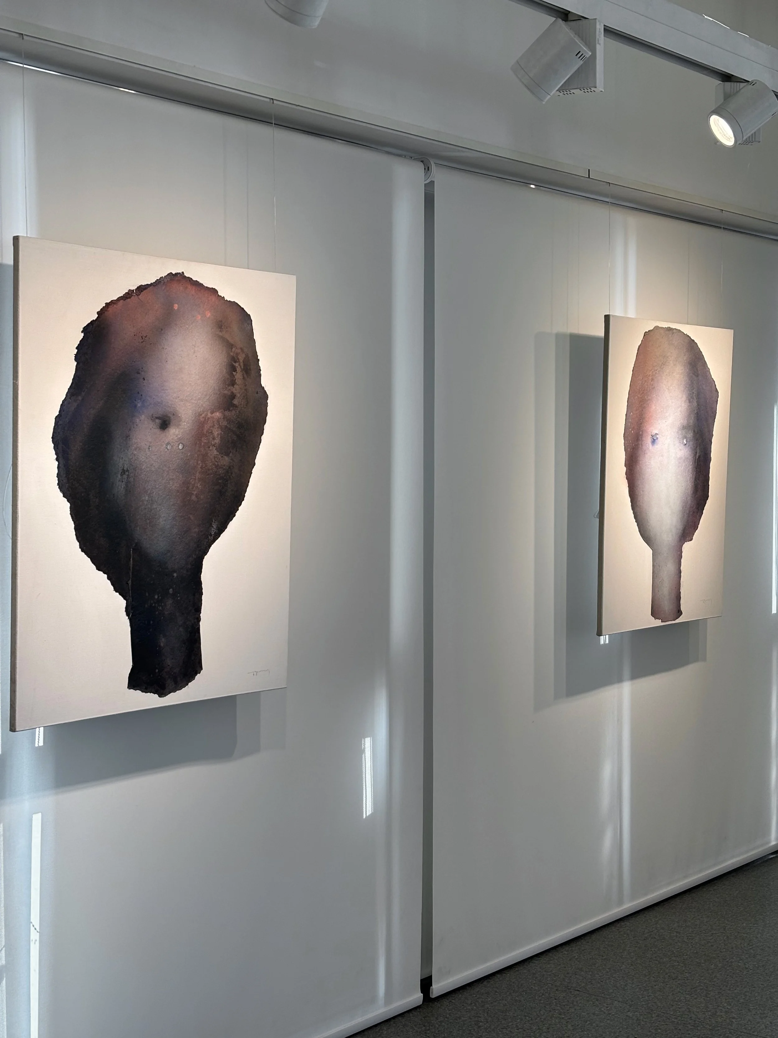 Two abstract face portraits on canvas displayed in an art gallery with white walls and track lighting.