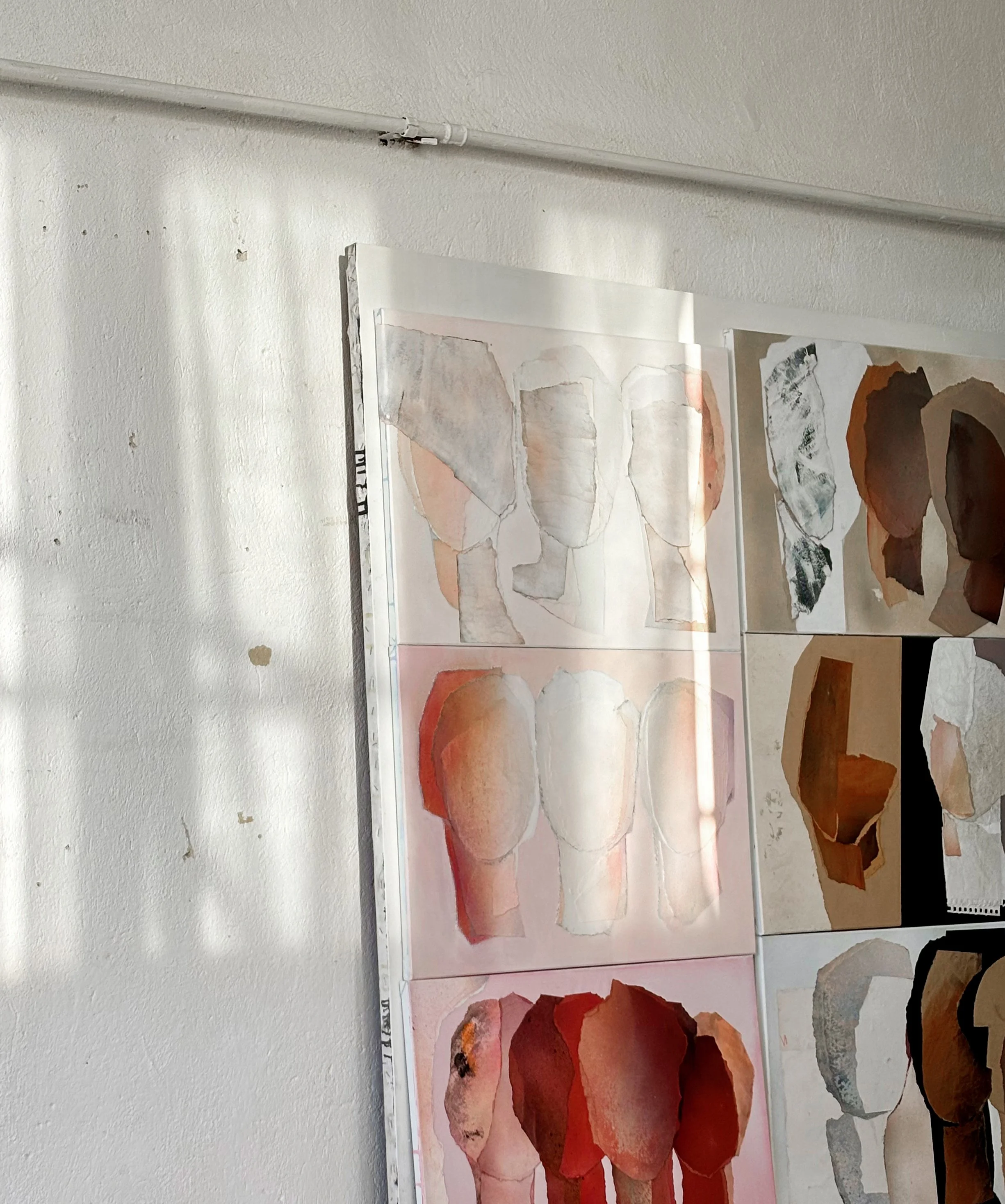Several abstract paintings of human torsos and faces on display in an art studio, with a white wall and a visible fluorescent light fixture in the background.