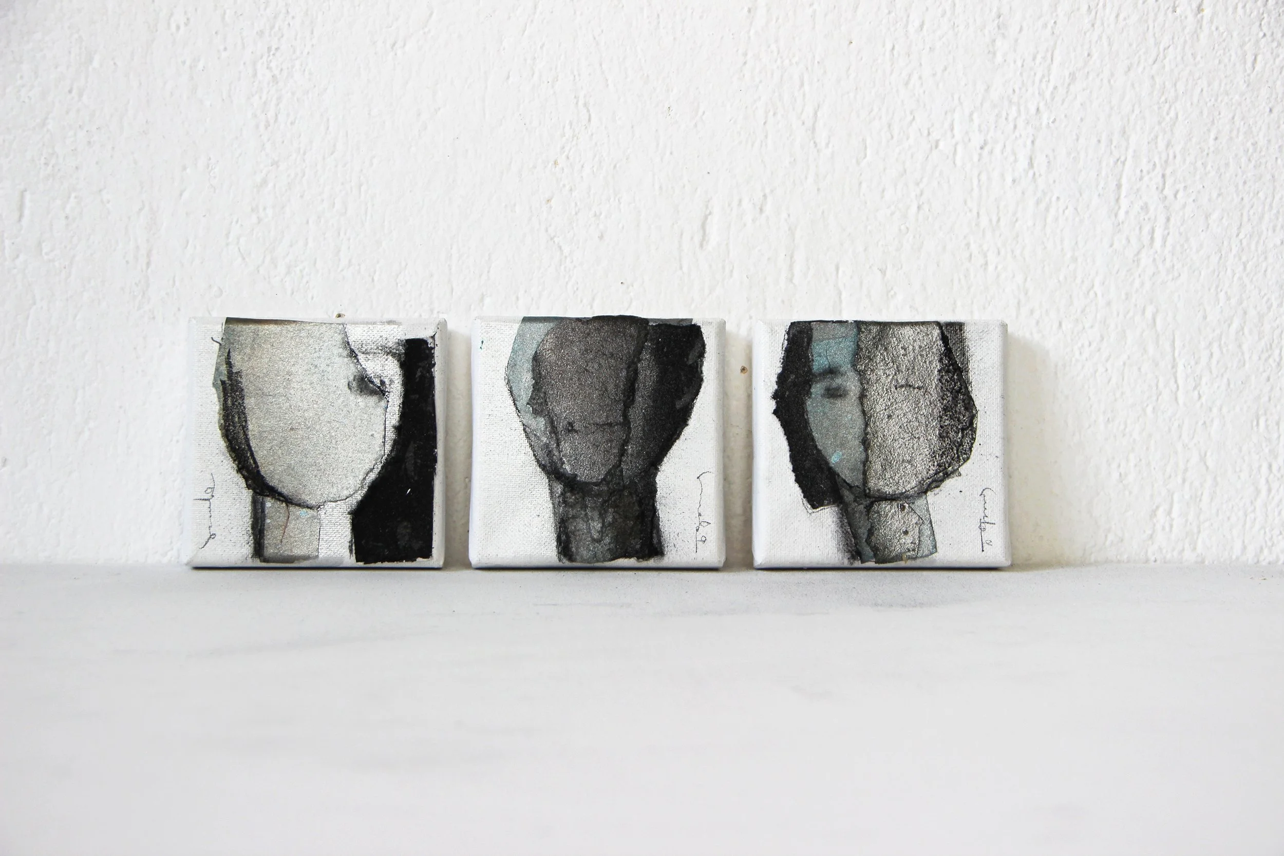 Three small abstract paintings on a white wall, each featuring a bottle shape with different black and gray watercolor patterns.
