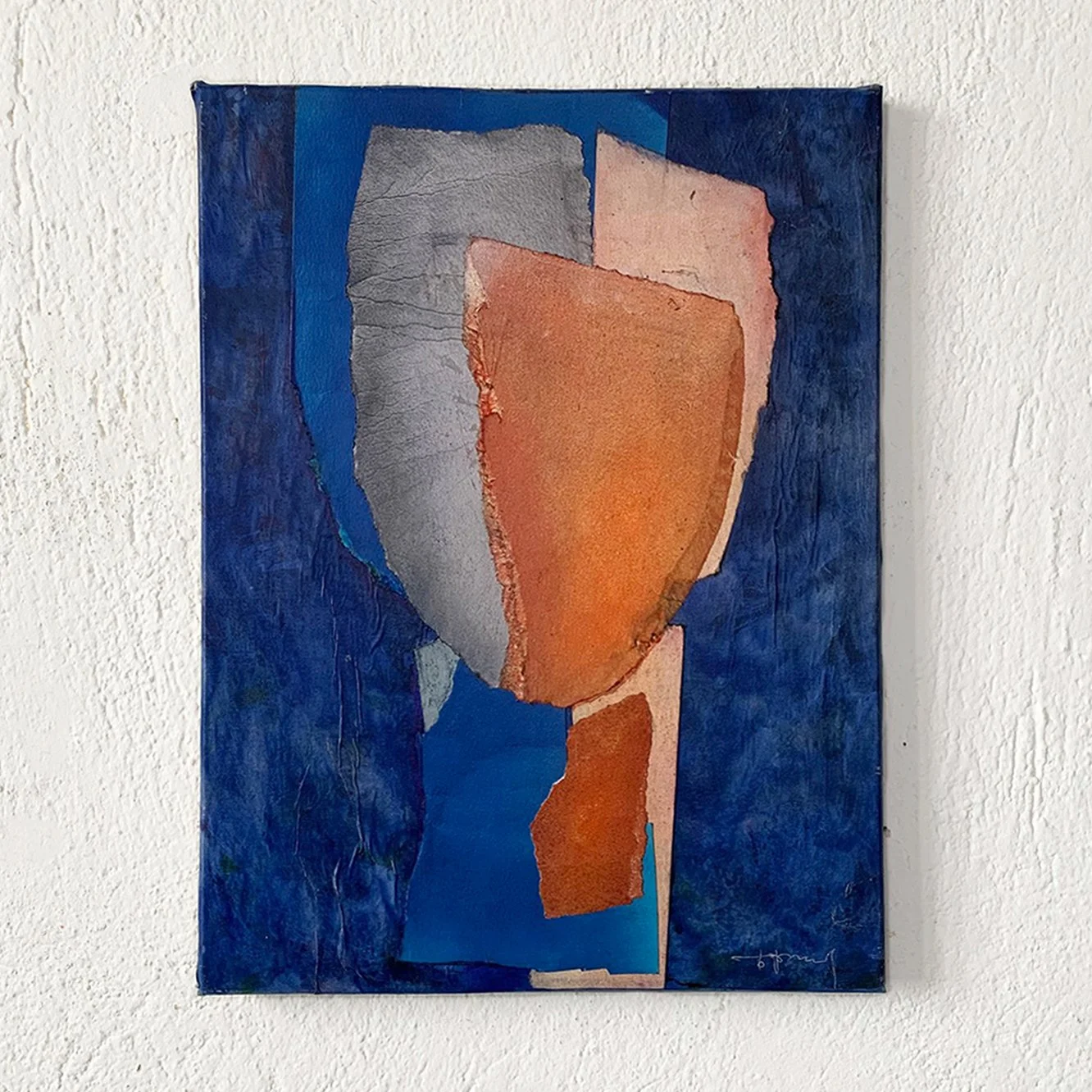 Abstract painting with irregularly shaped patches of blue, gray, orange, and pink on a white wall.