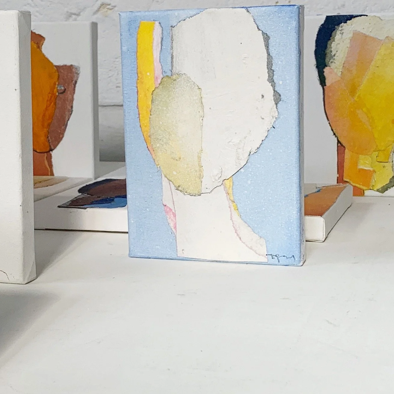 Watercolor portrait of a faceless figure with a blue background, yellow and pink accents, and abstract shapes.