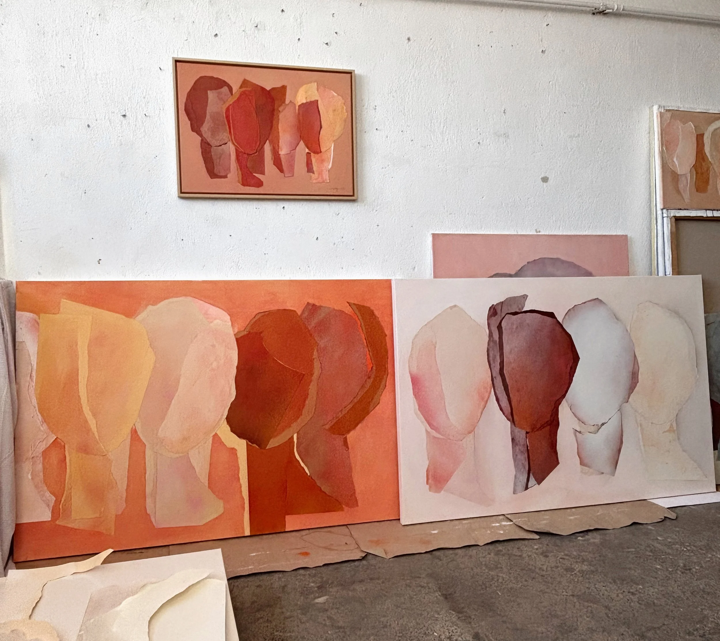 Multiple abstract paintings of human profiles in warm tones, displayed on the floor leaning against a wall