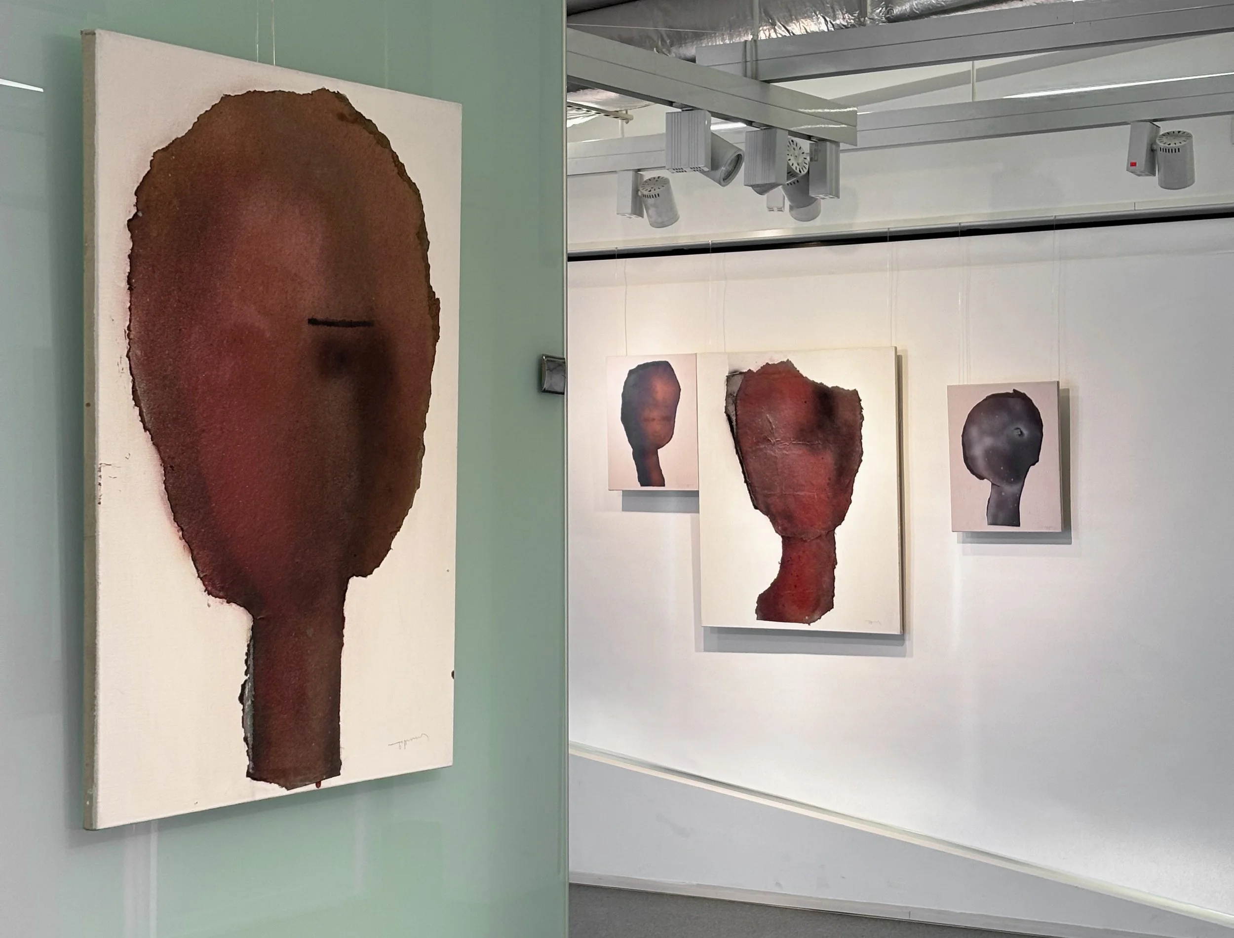Art gallery display of abstract portrait paintings of faces with simplified features in earthy tones.