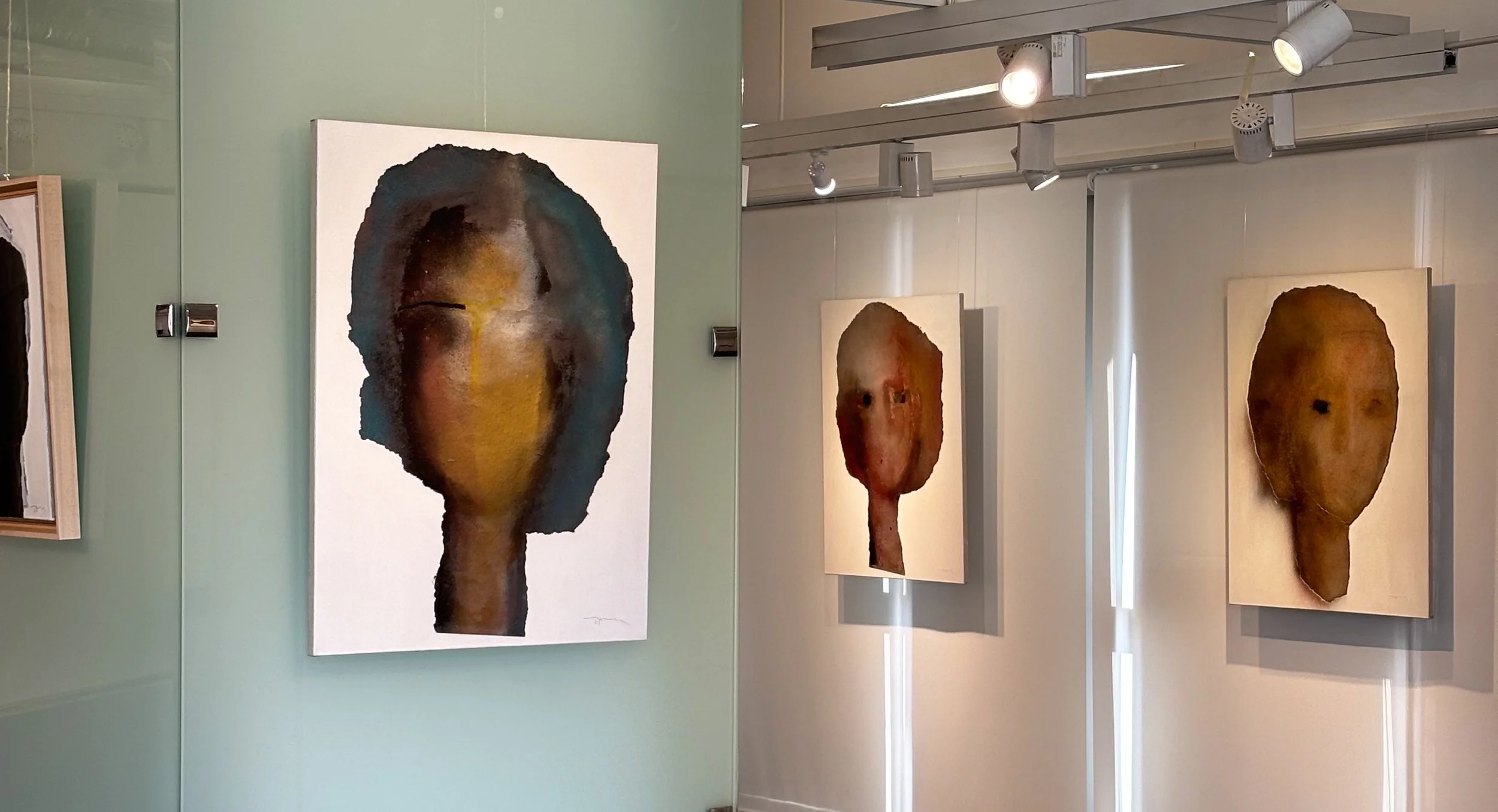 Art gallery with paintings of abstract, faceless portraits on white walls, featuring textured, earthy tones and eye-catching brushstrokes.