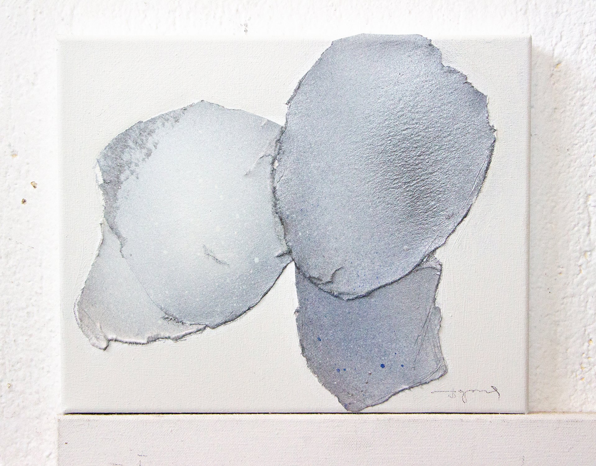 Abstract painting with three textured, oval shapes in shades of gray on a white background.
