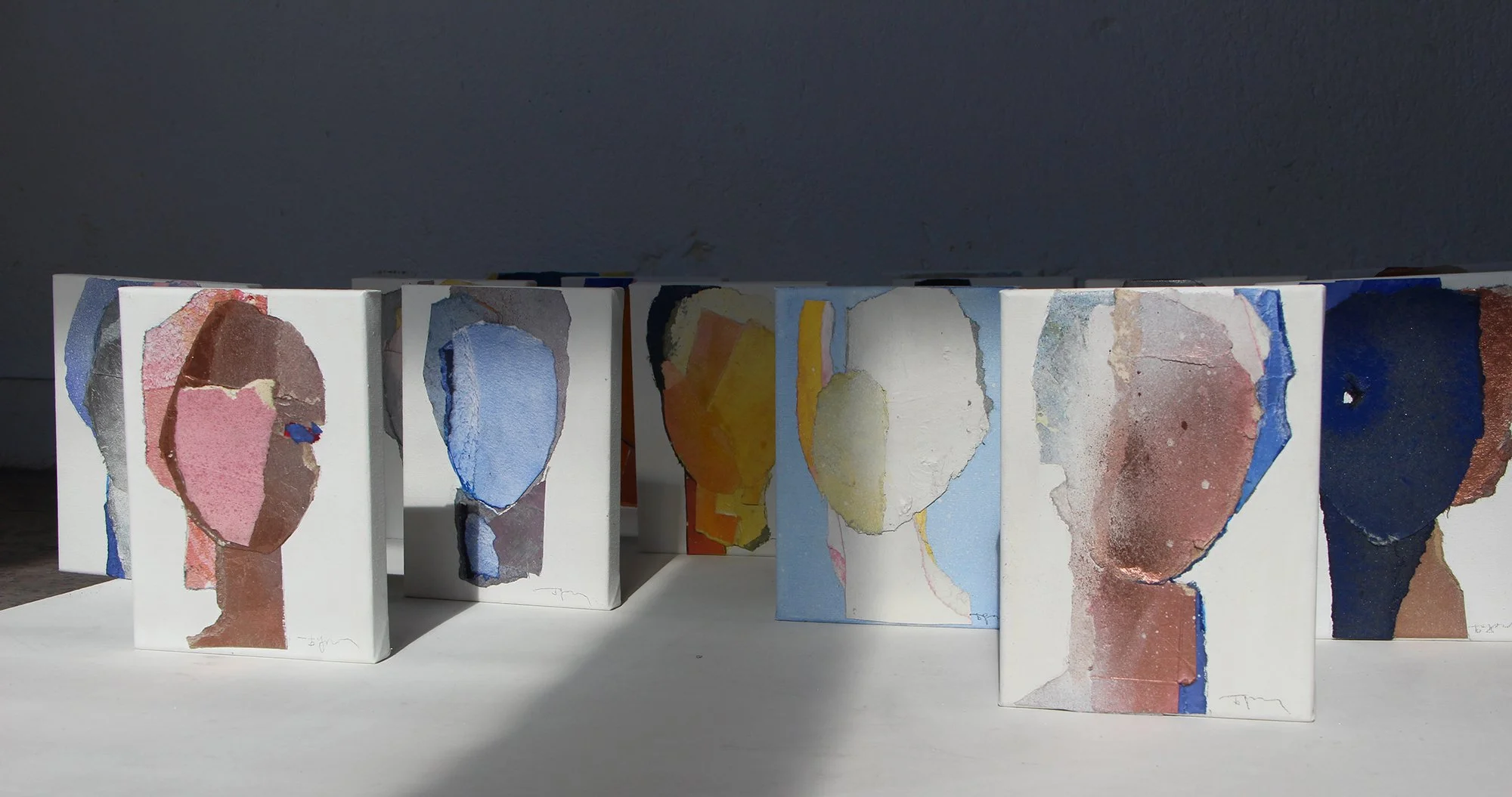 Multiple small abstract paintings with colorful, torn paper designs, arranged on a white surface.