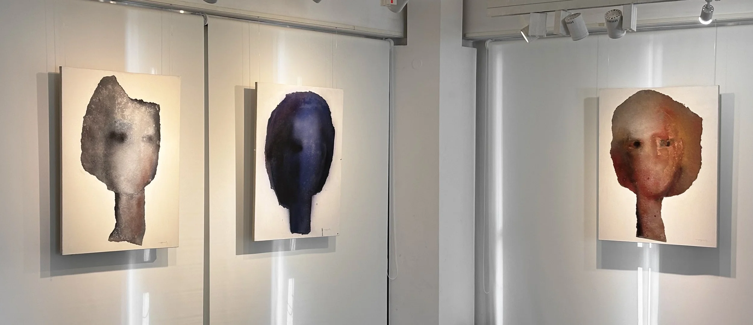 Art gallery with three abstract portrait paintings on white walls, each depicting a human face with a textured, distorted appearance.