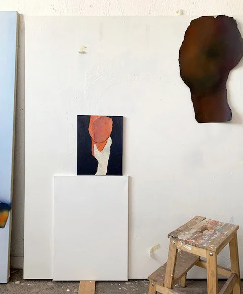 Empty art studio with a white wall, three canvases leaning against the wall, and a small wooden step stool.