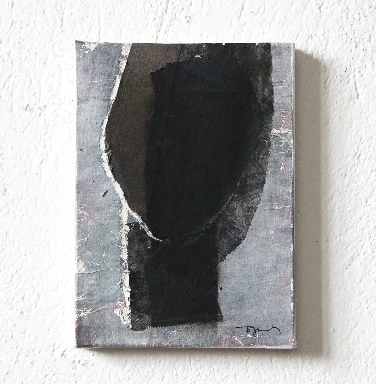 Abstract artwork on a rectangular canvas featuring dark, textured shapes in black and gray tones, mounted on a white wall.