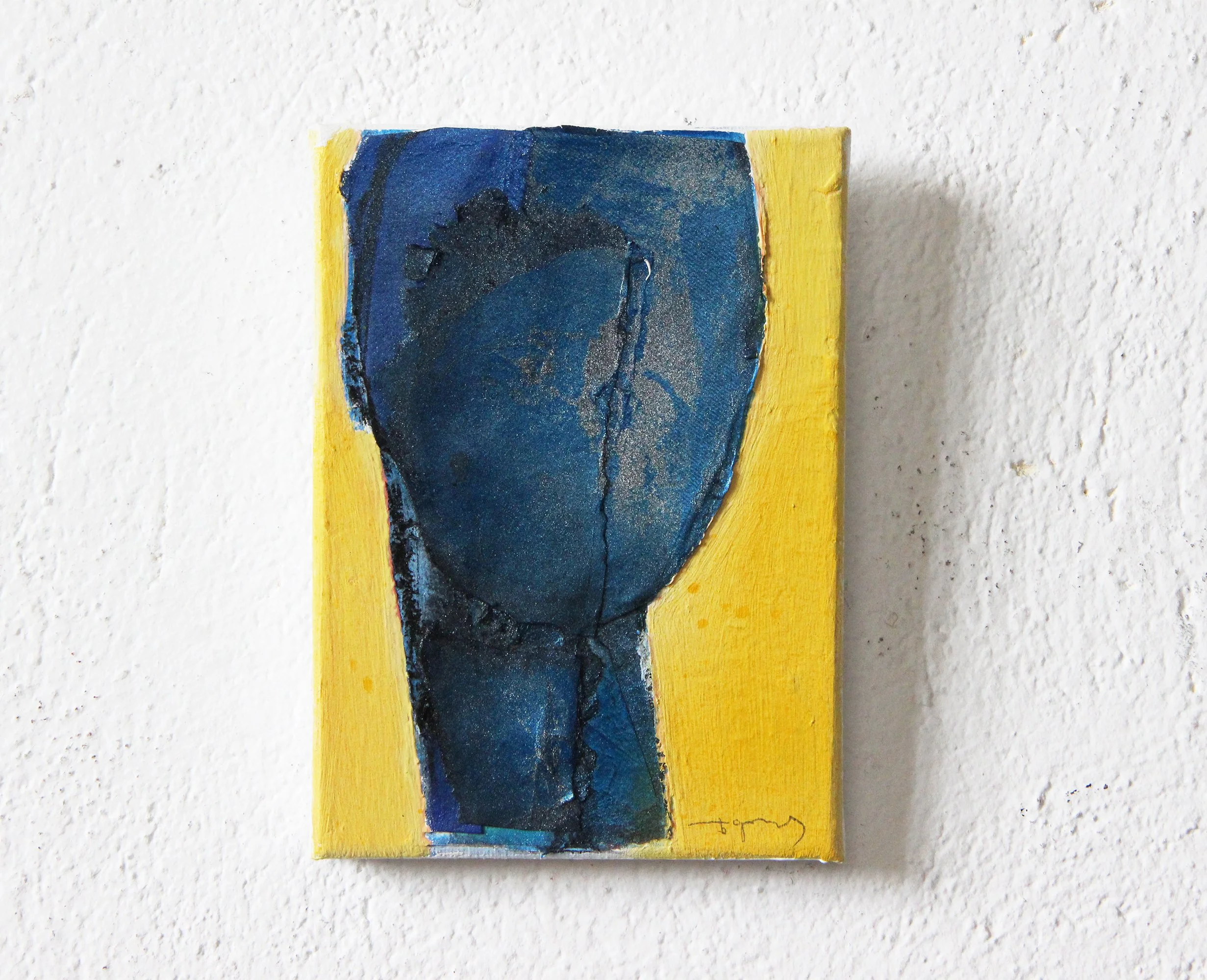 Abstract painting on small canvas featuring a dark blue face with closed eyes against a yellow background, hung on a white textured wall.