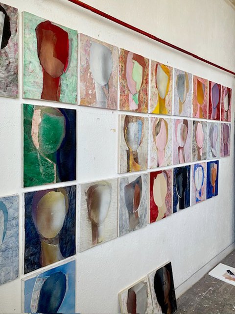 A wall display of multiple abstract paintings, each depicting a simplified human head in various colors.