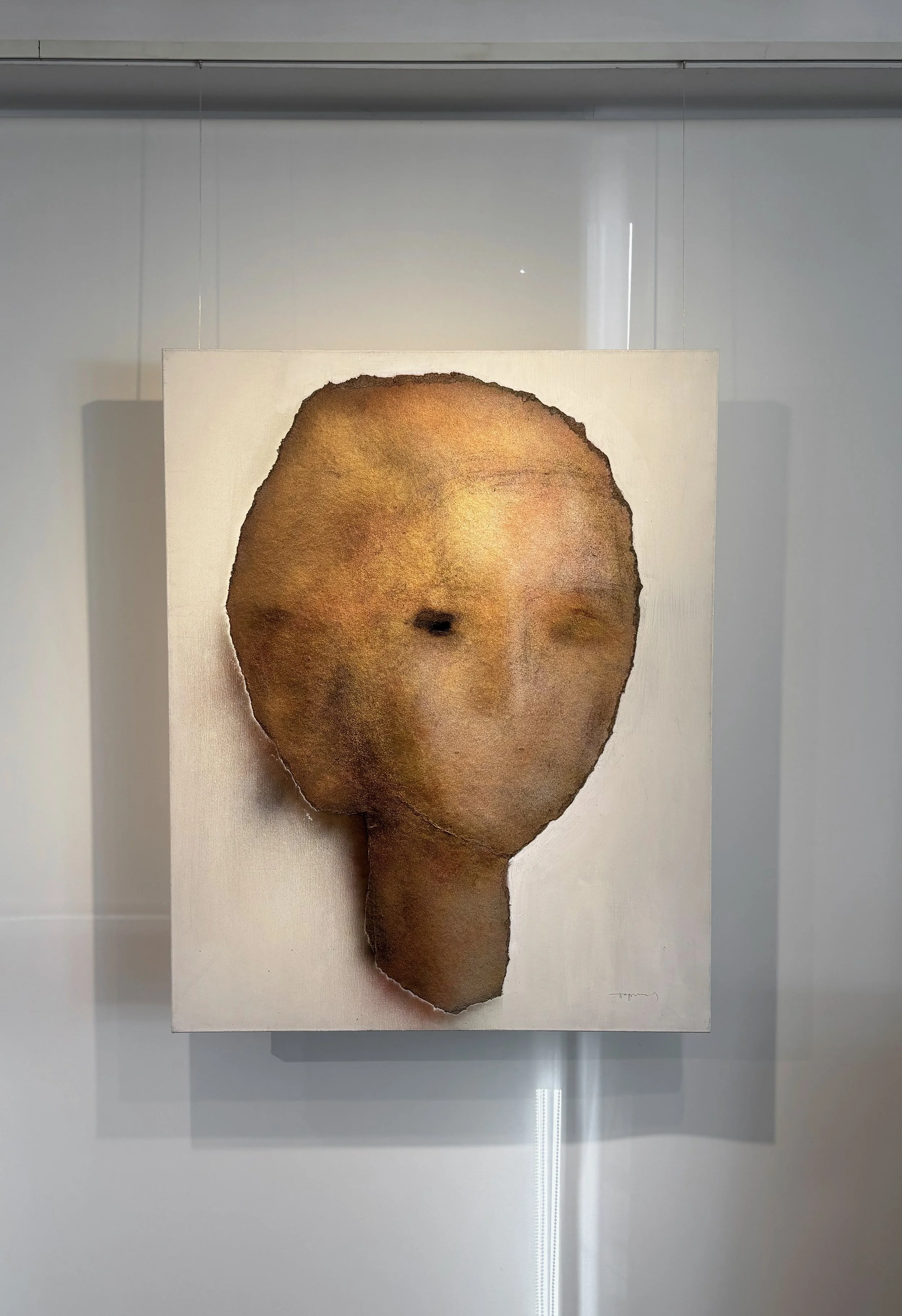 An artwork featuring a portrait of a human face with simplified, abstract features, in earthy tones, created on textured paper with torn edges.
