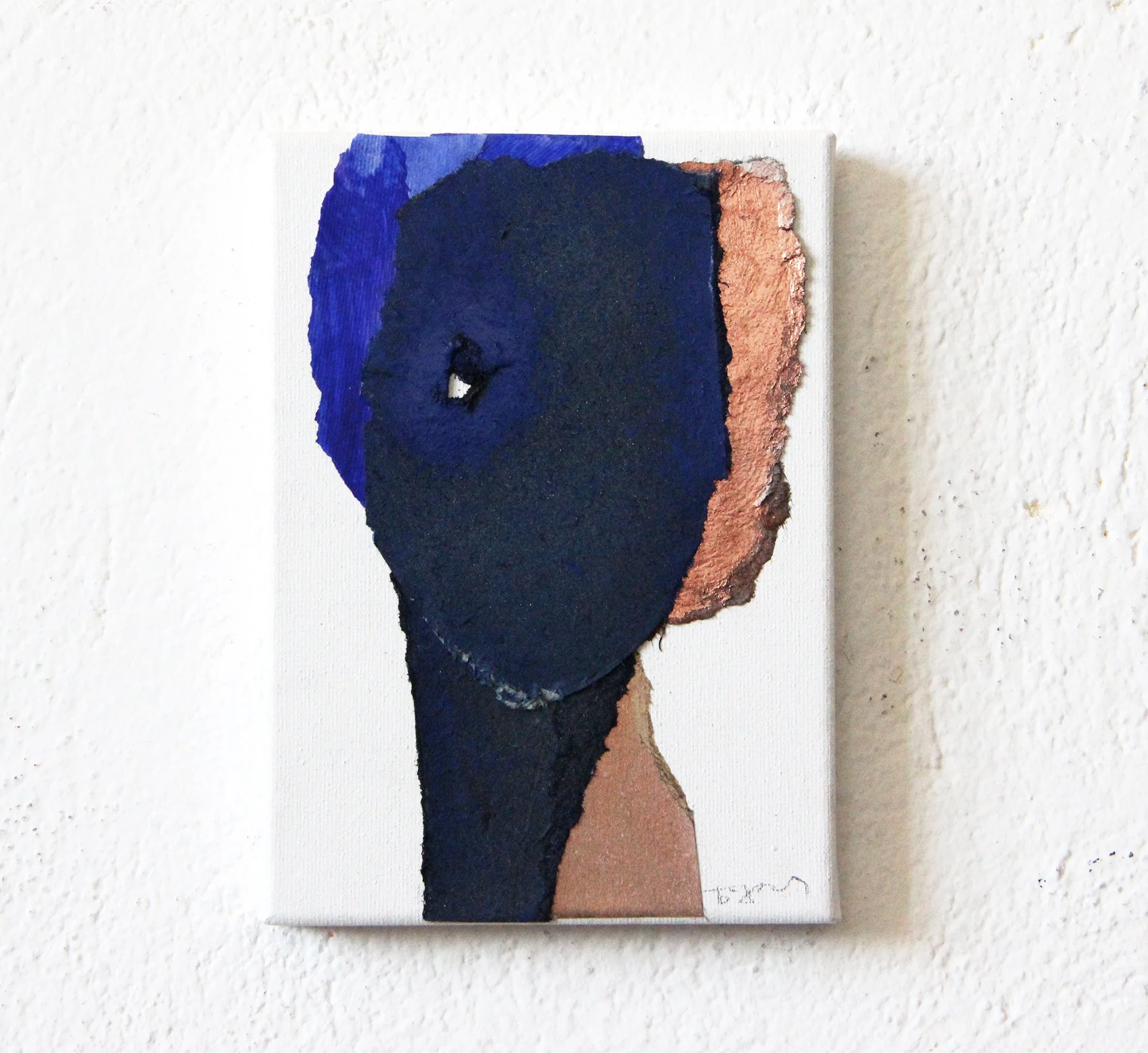Abstract mixed media artwork of a human face with a blue mask covering one eye, composed of textured paint and collage elements on a white canvas, mounted on a textured white wall.