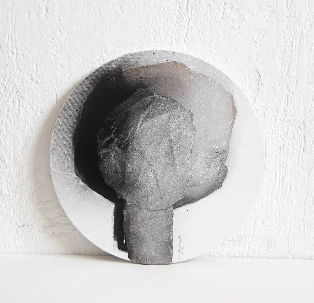 Black and white abstract painting of a tree on a round canvas, leaning on a white textured wall.