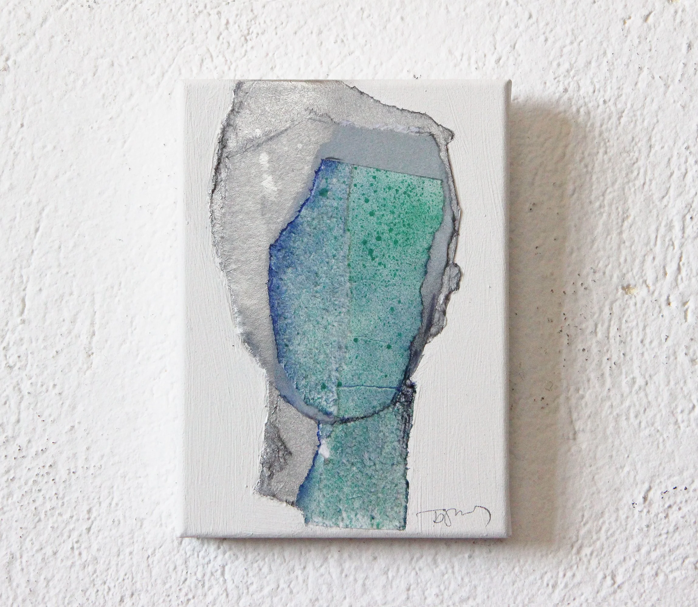 Abstract watercolor painting on a small canvas, featuring shades of blue, green, and gray, mounted on a white textured wall.