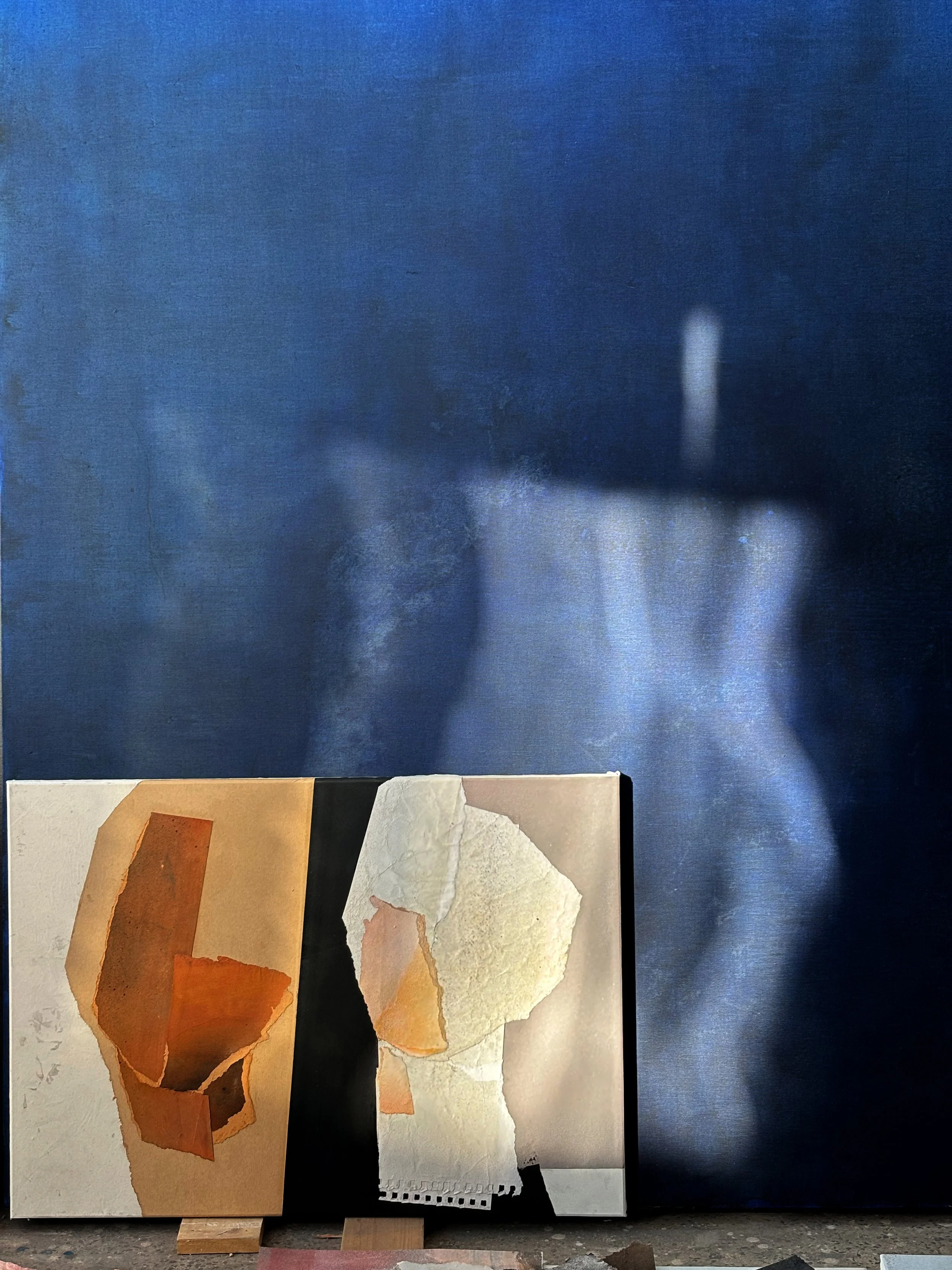 An abstract collage artwork featuring torn paper pieces in shades of orange, cream, and black, displayed against a textured blue background.
